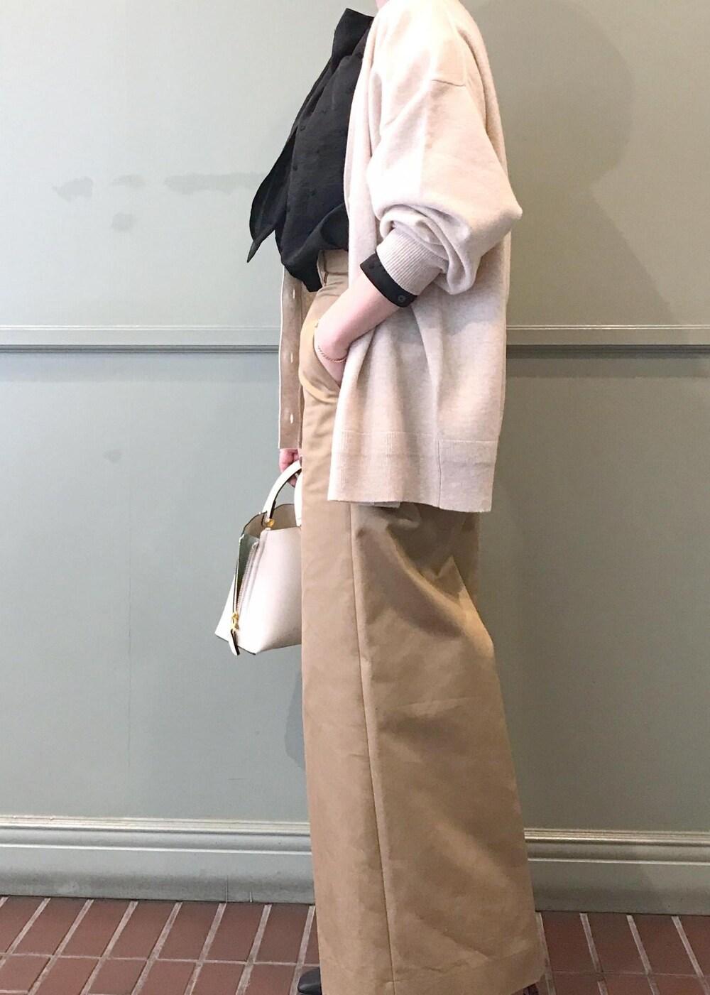 ホワイト系のハンドバッグ、ブラック系のブーツ、ベージュ系のチノパンツを着用したレディースの秋コーディネートの2枚目の写真