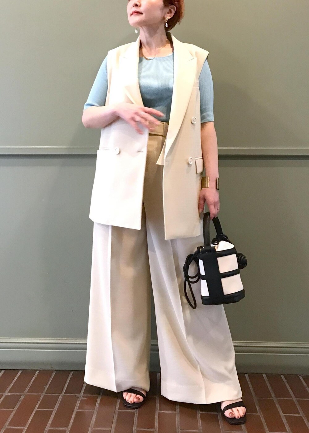ブラック系のハンドバッグ、ブラック系のサンダル、ホワイト系のベストを着用したレディースの春コーディネートの2枚目の写真