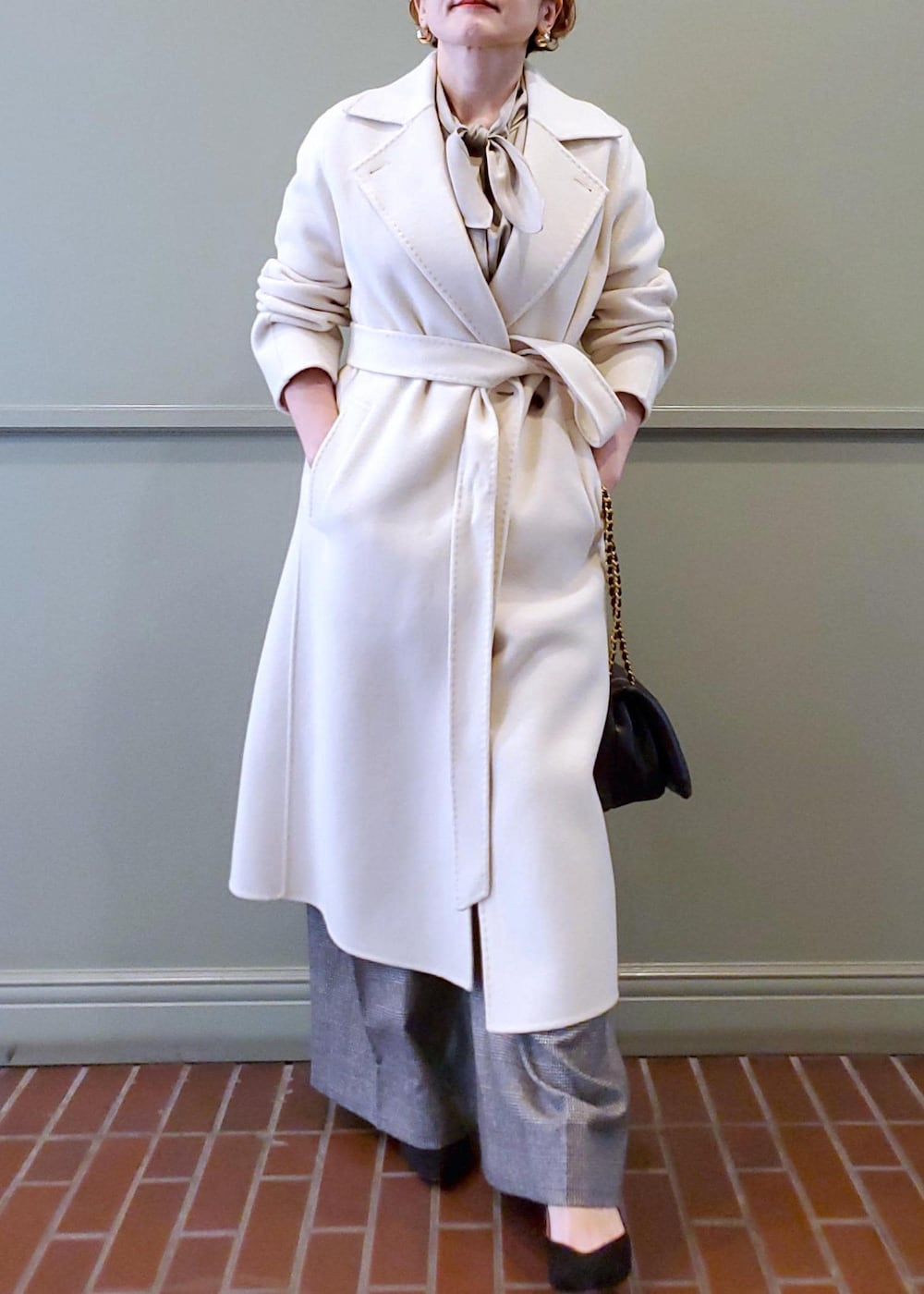 ブラック系のハンドバッグ、ホワイト系のチェスターコート、ベージュ系のシャツ/ブラウスを着用したレディースの秋コーディネートの3枚目の写真