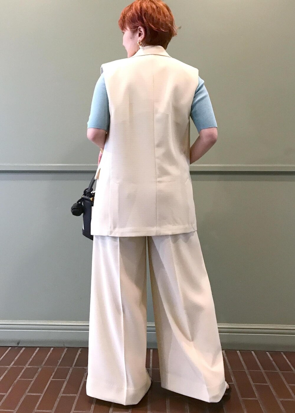 ブラック系のハンドバッグ、ブラック系のサンダル、ホワイト系のベストを着用したレディースの春コーディネートの4枚目の写真