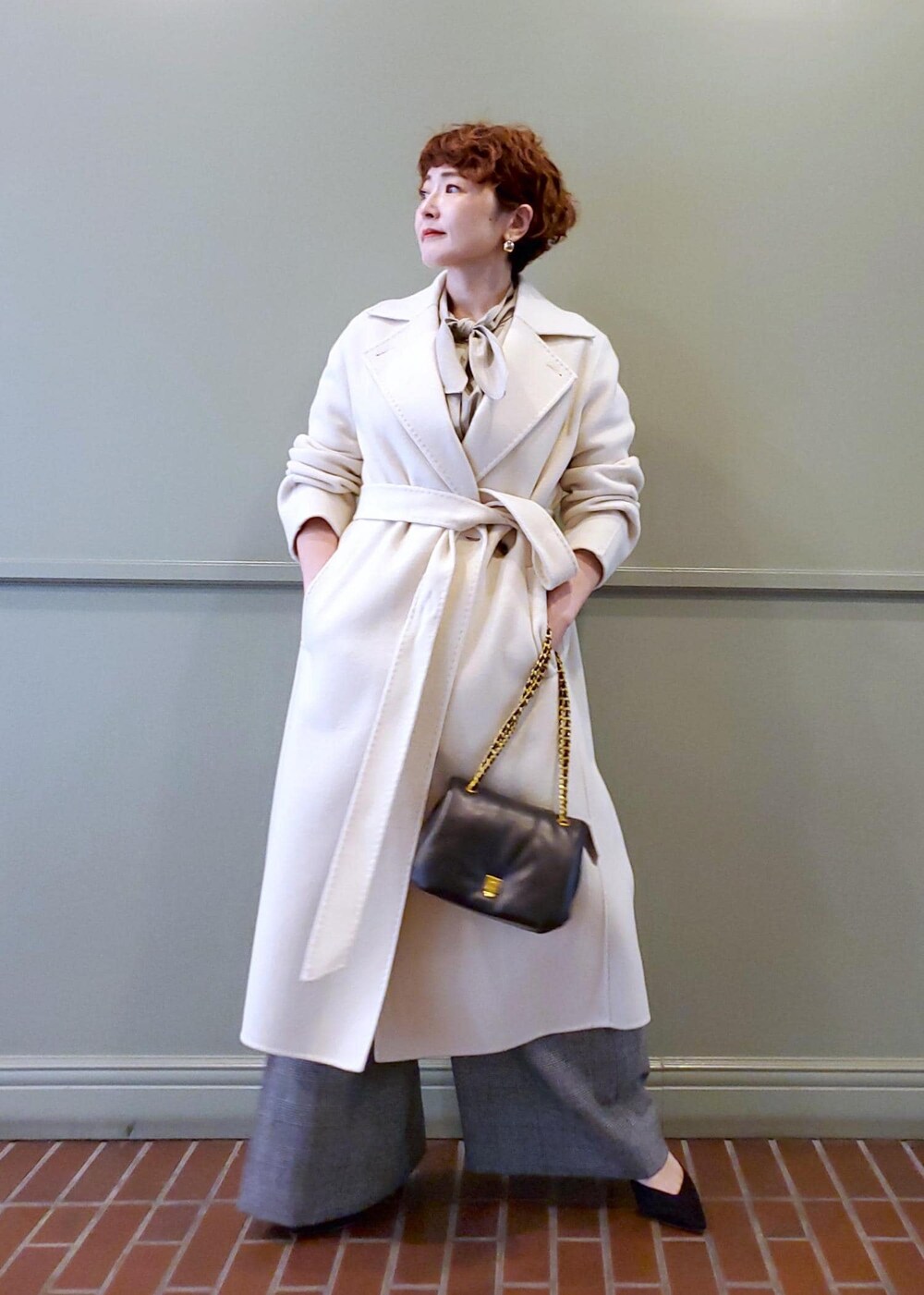 ブラック系のハンドバッグ、ホワイト系のチェスターコート、ベージュ系のシャツ/ブラウスを着用したレディースの秋コーディネートの2枚目の写真