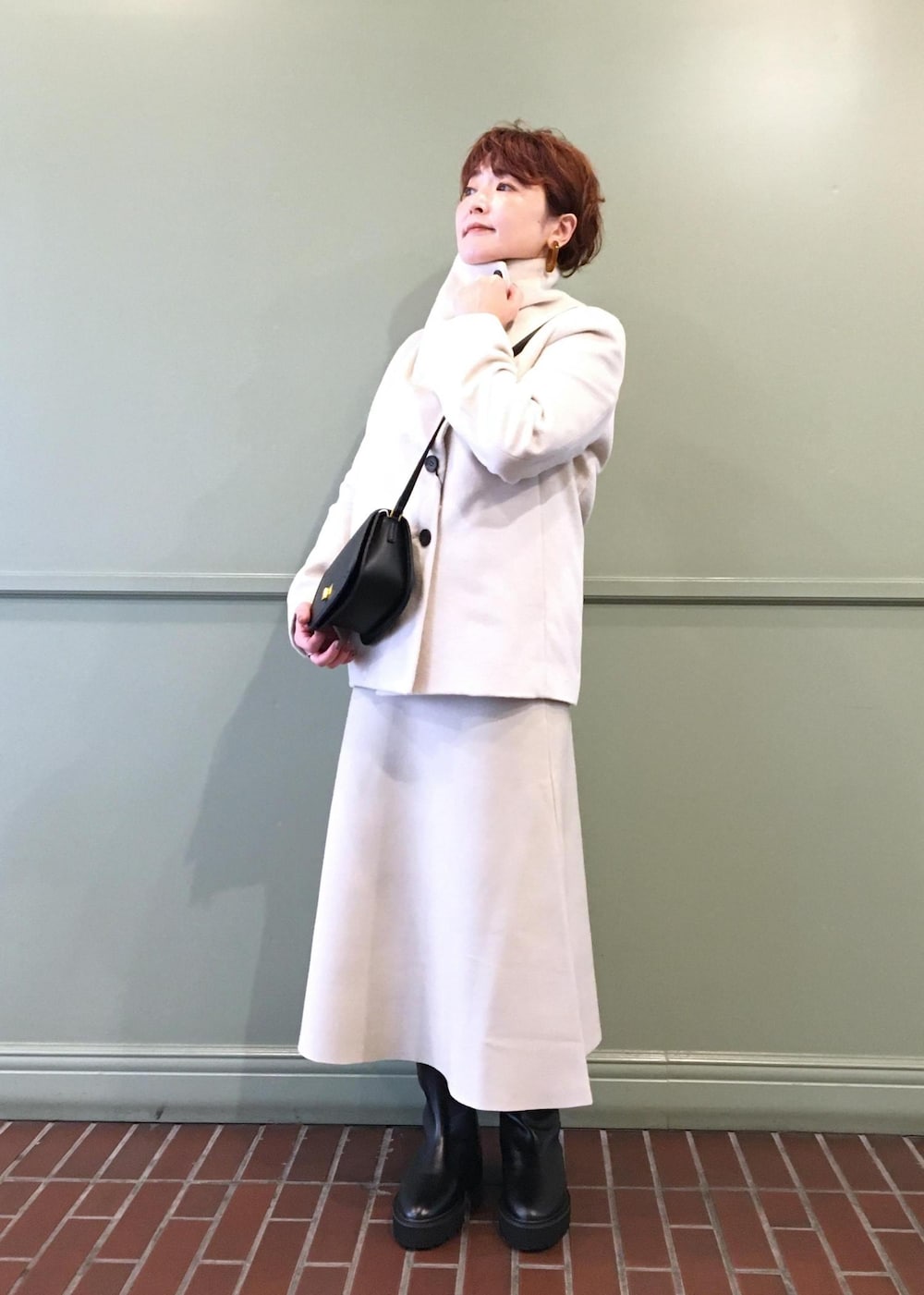 ブラック系のショルダーバッグ、ホワイト系のステンカラーコート、ブラック系のブーツを着用したレディースの秋コーディネートの2枚目の写真
