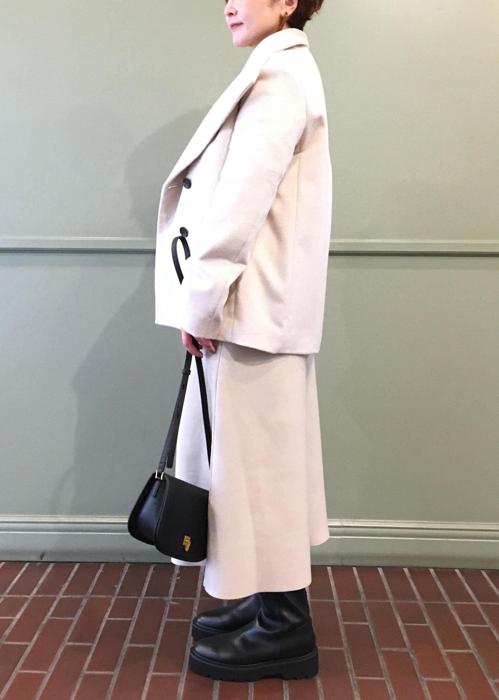 ブラック系のショルダーバッグ、ホワイト系のステンカラーコート、ブラック系のブーツを着用したレディースの秋コーディネートの4枚目の写真