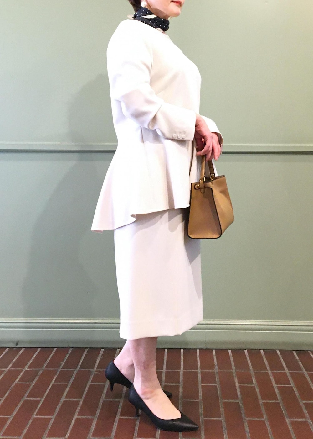 ブラック系のパンプス、ベージュ系のショルダーバッグ、ベージュ系のスカートを着用したレディースの冬コーディネートの2枚目の写真