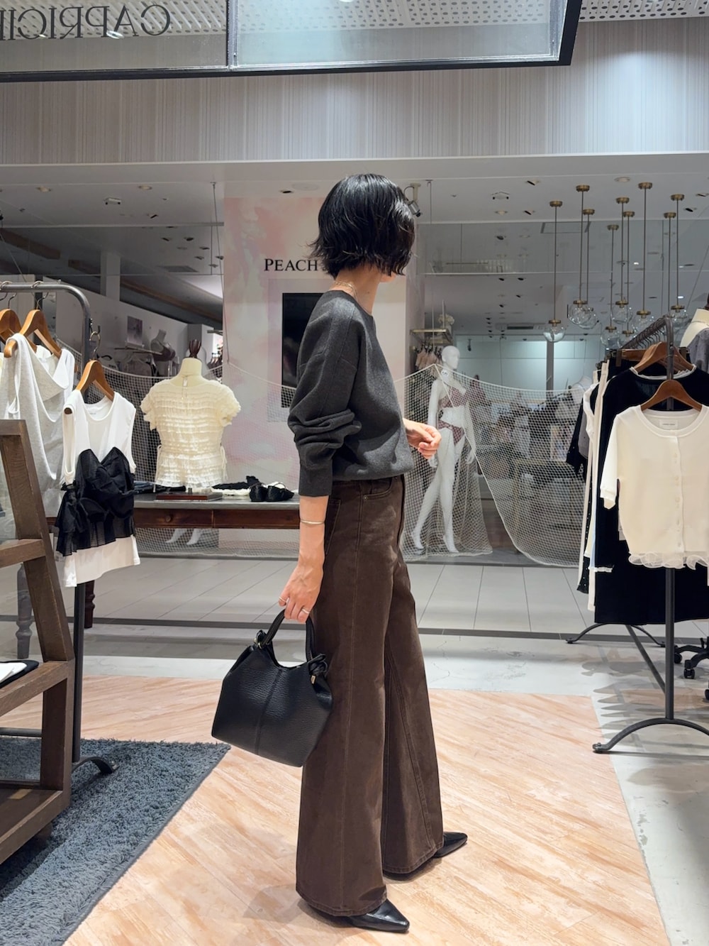 グレー系のニット/セーター、ブラウン系のデニムパンツ、ブラック系のショルダーバッグを着用したレディースの秋コーディネートの2枚目の写真