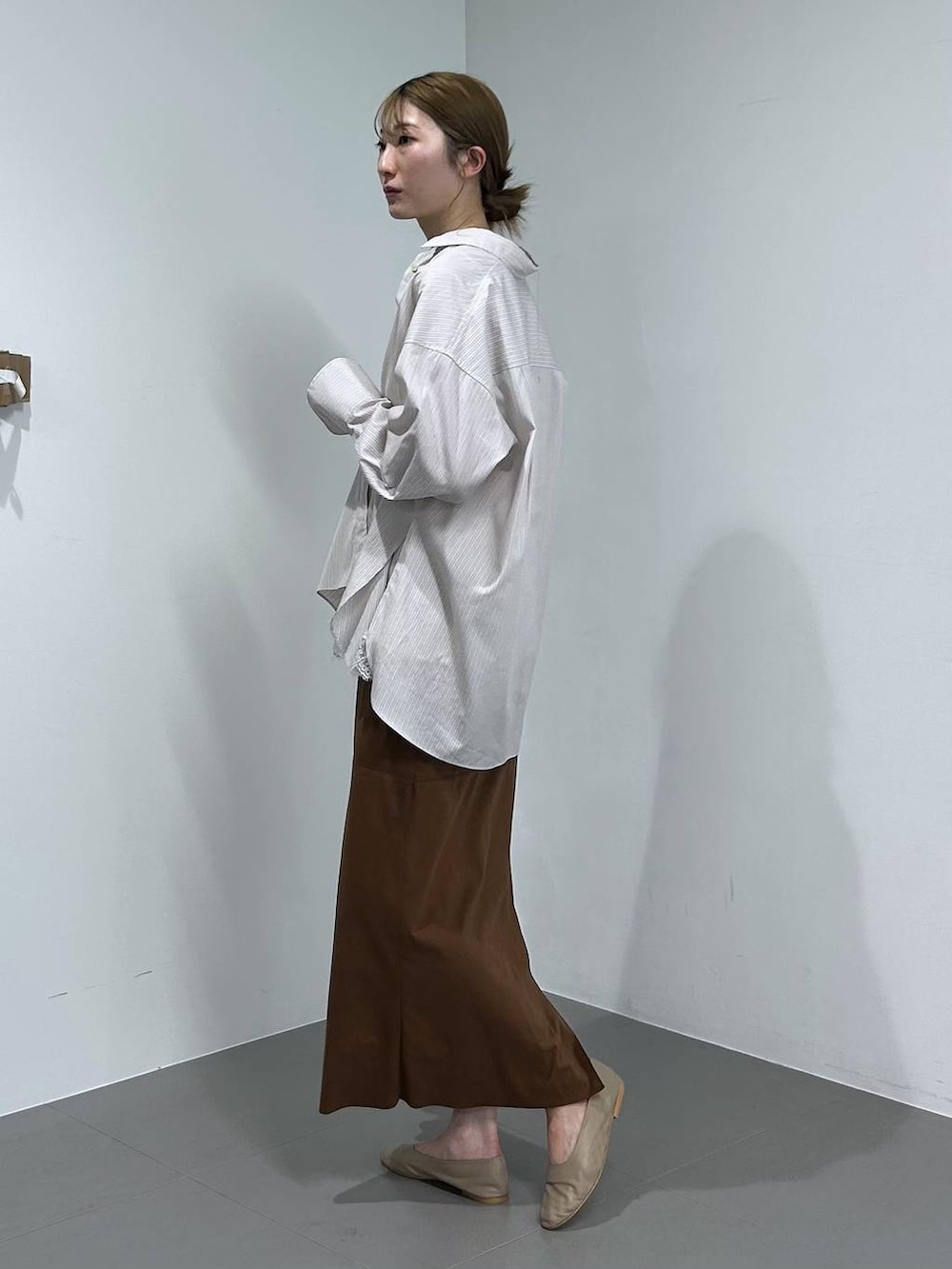 イエロー系のスカート、ベージュ系のシャツ/ブラウス、ブラウン系のショルダーバッグを着用したレディースの冬コーディネートの2枚目の写真