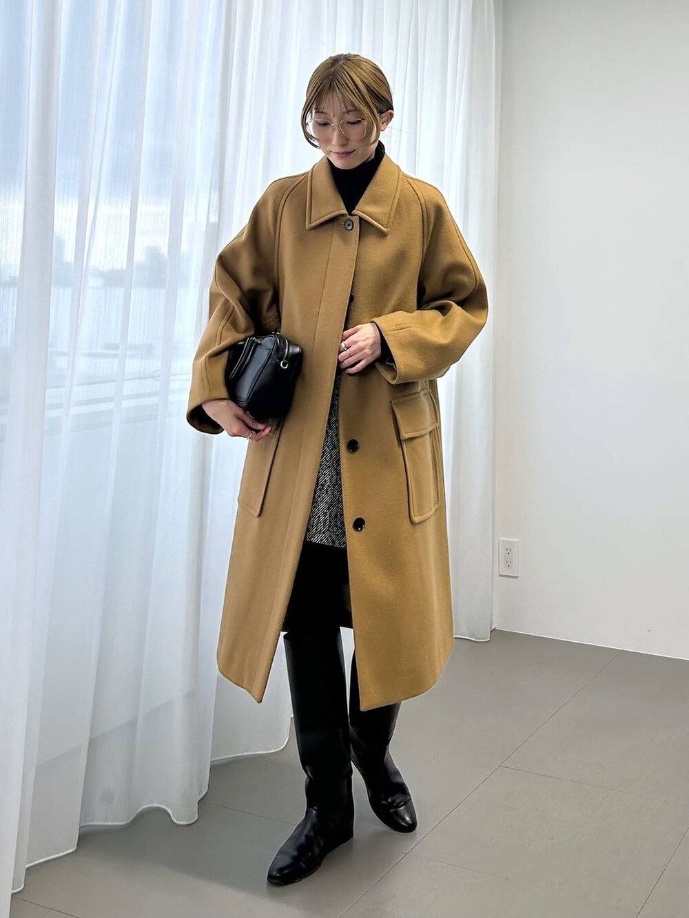 イエロー系のステンカラーコート、ブラック系のボストンバッグ、ブラック系のニット/セーターを着用したレディースの秋コーディネートの3枚目の写真