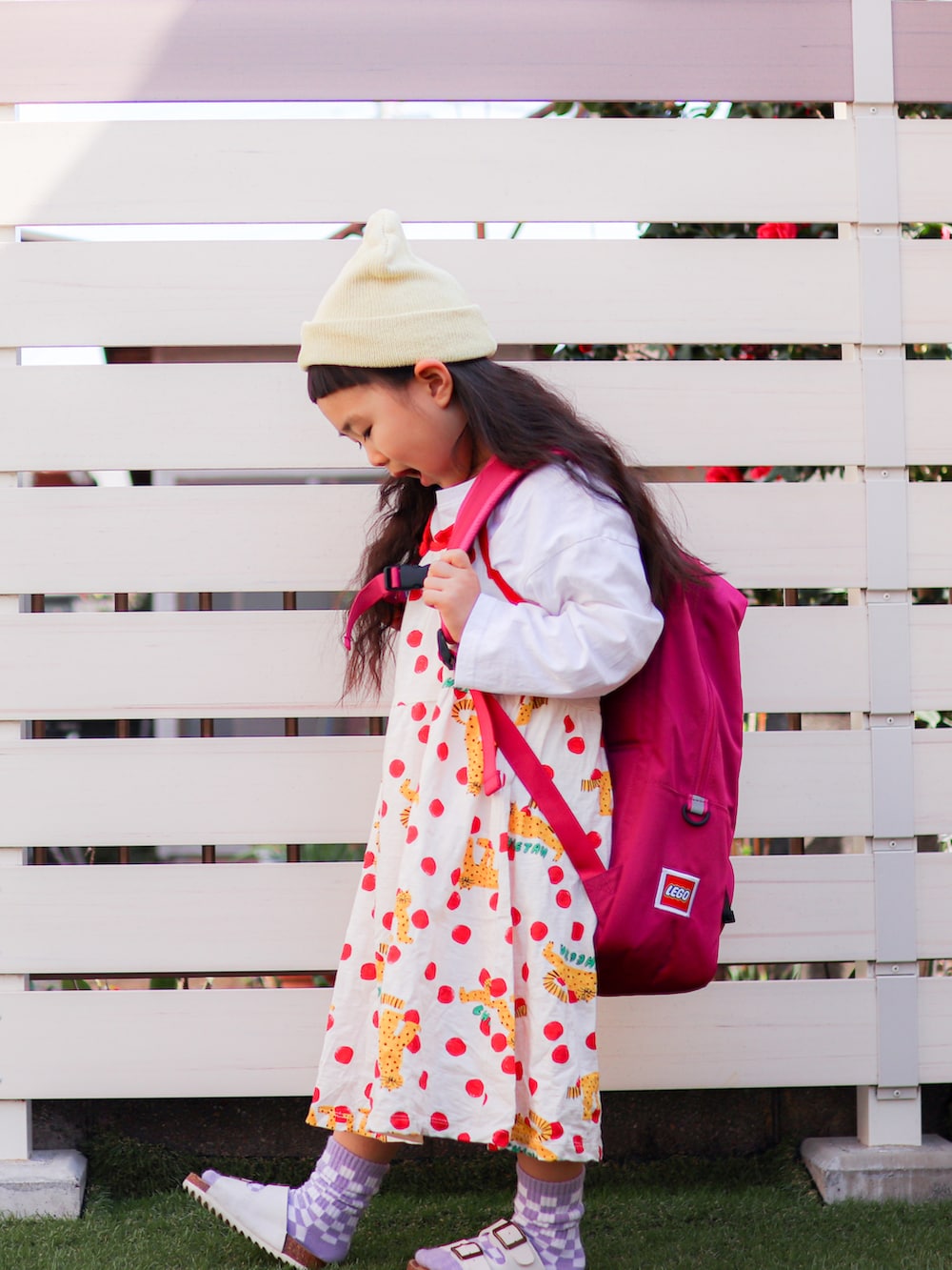 ホワイト系のワンピース、ピンク系のバックパック/リュック、イエロー系のニットキャップ/ビーニーを着用したキッズの春コーディネートの2枚目の写真