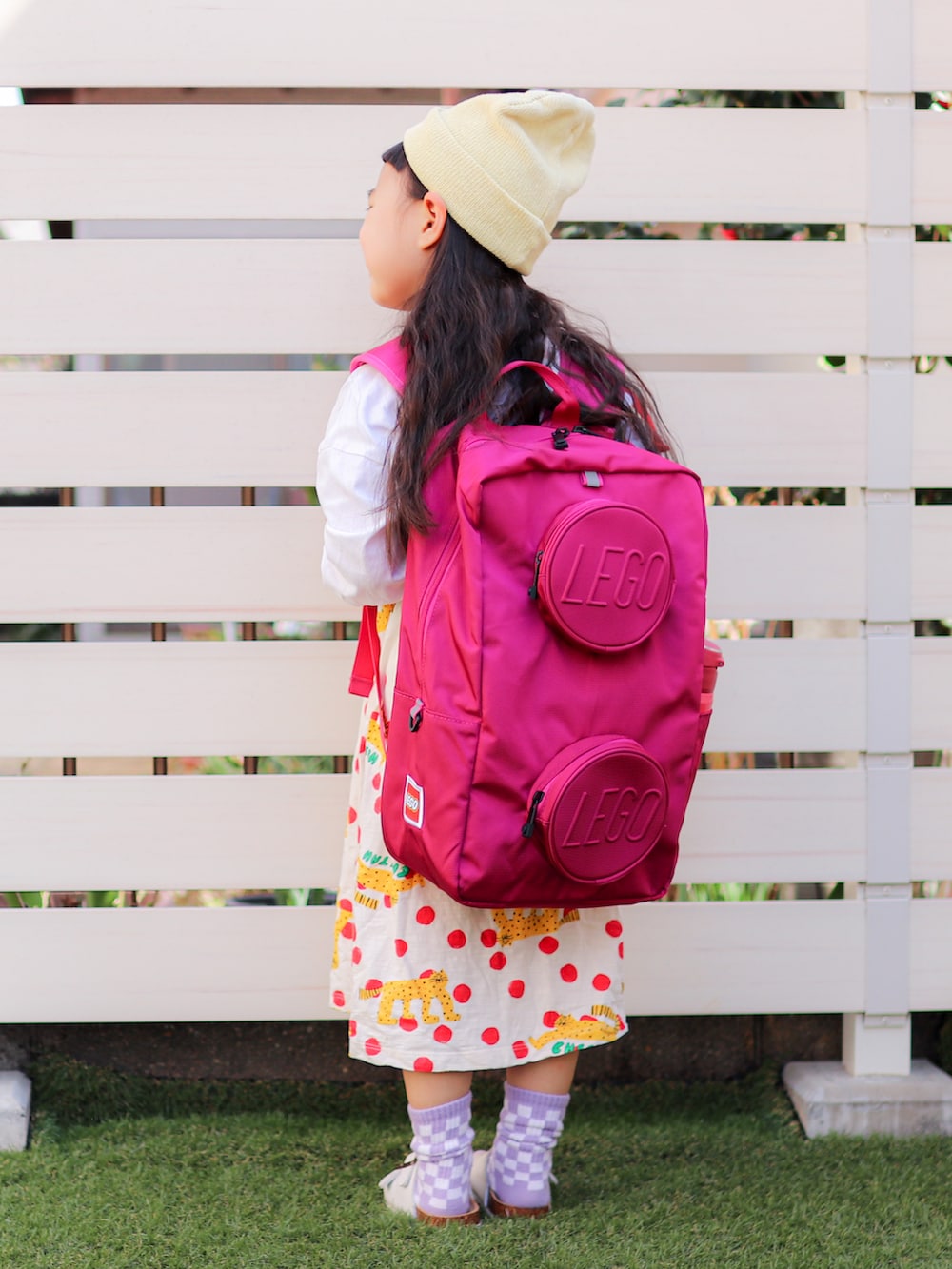 ホワイト系のワンピース、ピンク系のバックパック/リュック、イエロー系のニットキャップ/ビーニーを着用したキッズの春コーディネートの3枚目の写真