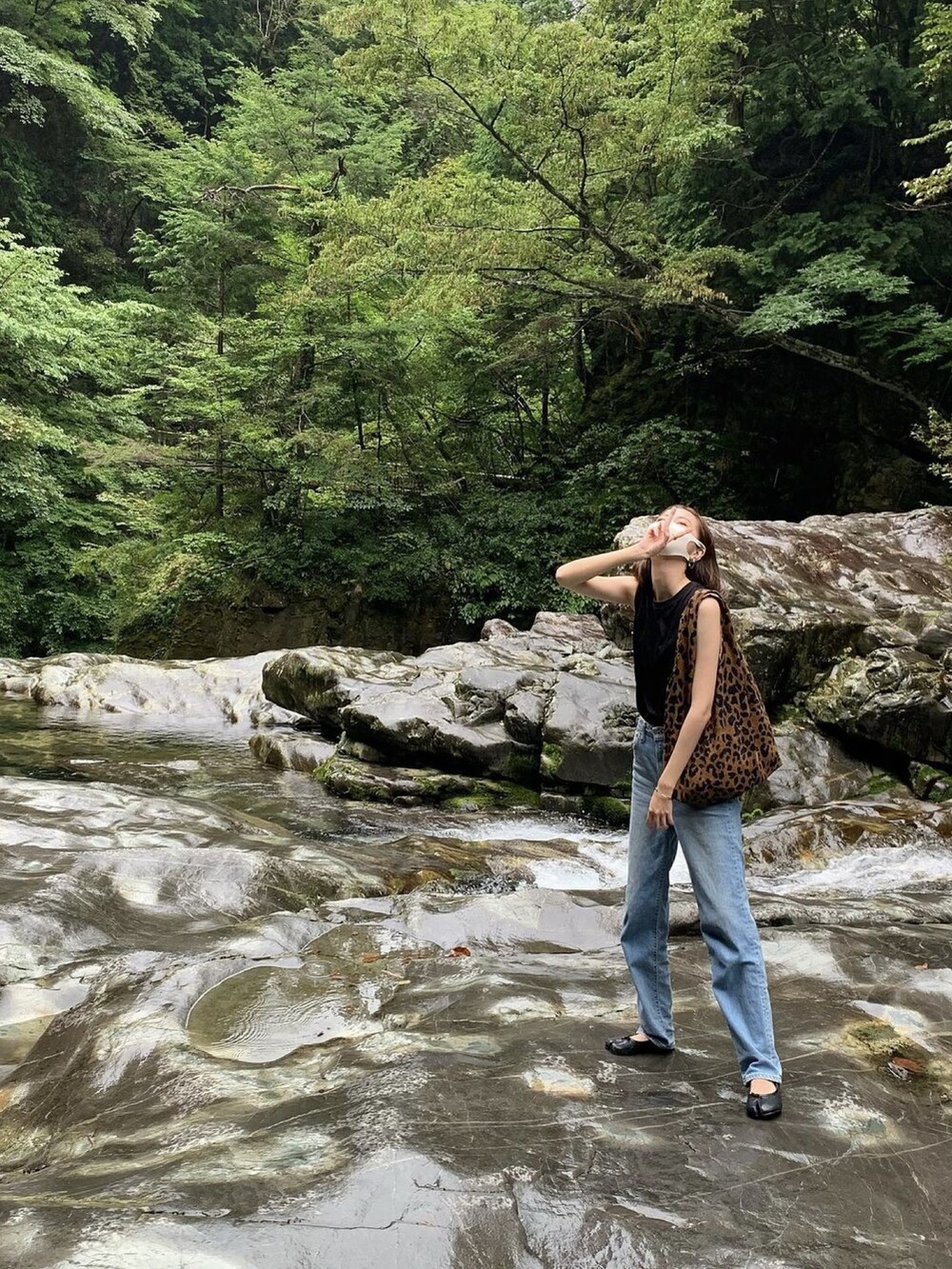 ブルー系のデニムパンツ、ブラック系のトップス、ブラウン系のバッグを着用したレディースの夏コーディネートの2枚目の写真