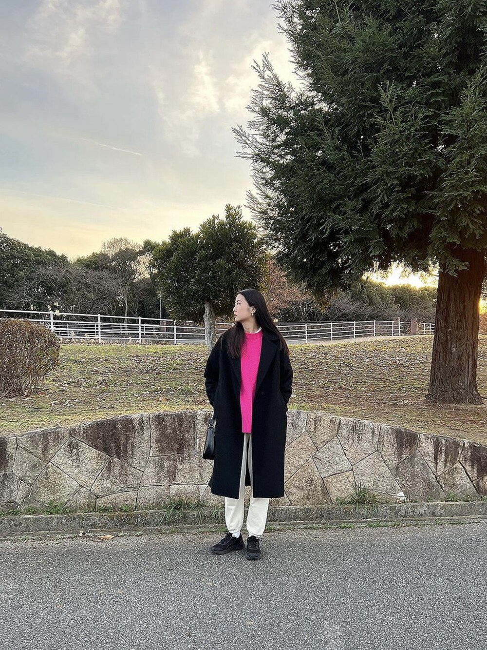 ブラック系のチェスターコート、ピンク系のニット/セーター、ホワイト系のスウェットパンツを着用したレディースの冬コーディネートの2枚目の写真