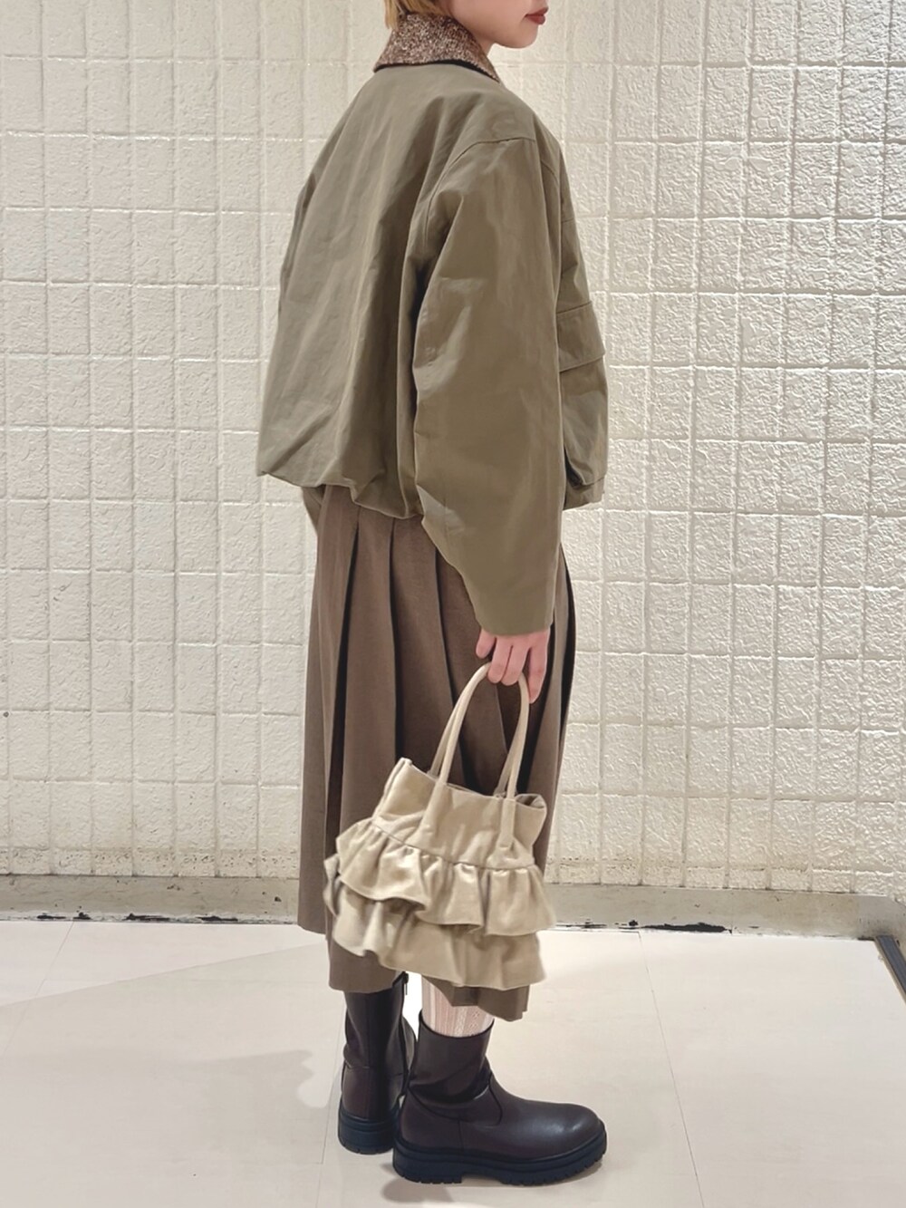 グリーン系のブルゾン、ブラウン系のスカート、ベージュ系のハンドバッグを着用したレディースの冬コーディネートの6枚目の写真