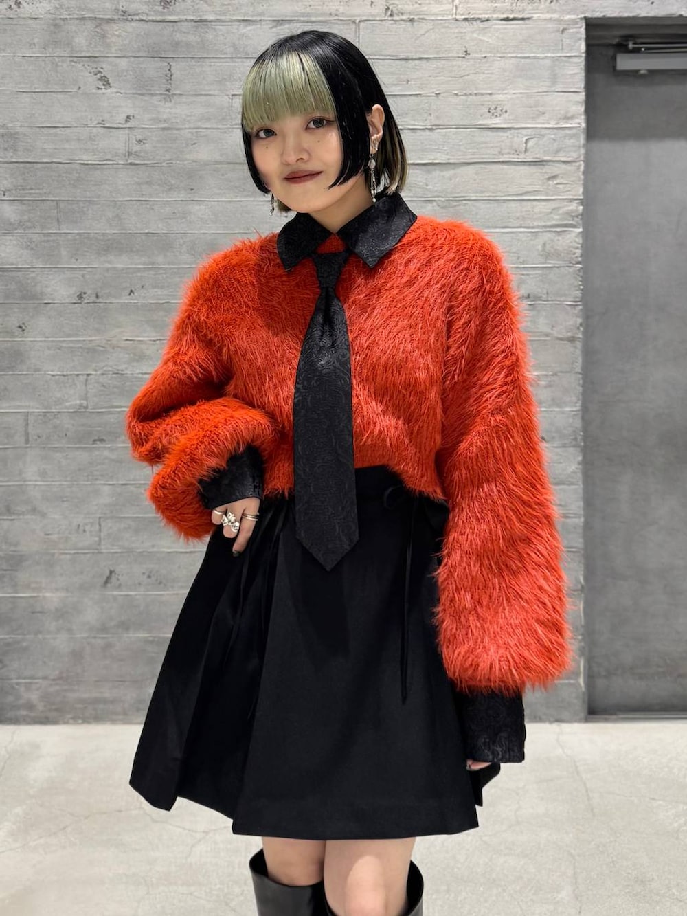 オレンジ系のニット/セーター、ブラック系のシャツ/ブラウス、ブラック系のブーツを着用したレディースの冬コーディネートの2枚目の写真