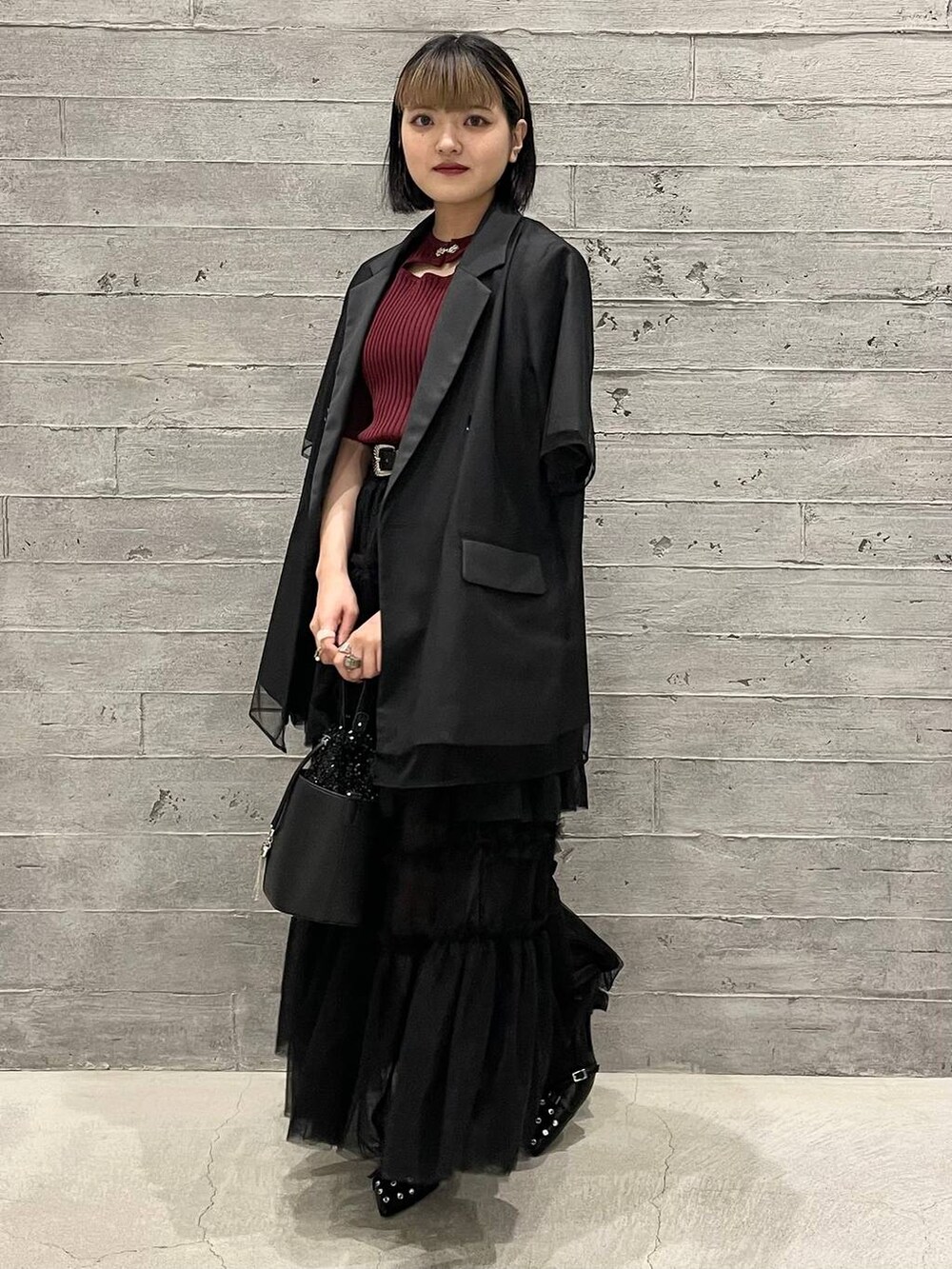 レッド系のニット/セーター、ブラック系のショルダーバッグ、ブラック系のパンプスを着用したレディースの夏コーディネートの3枚目の写真