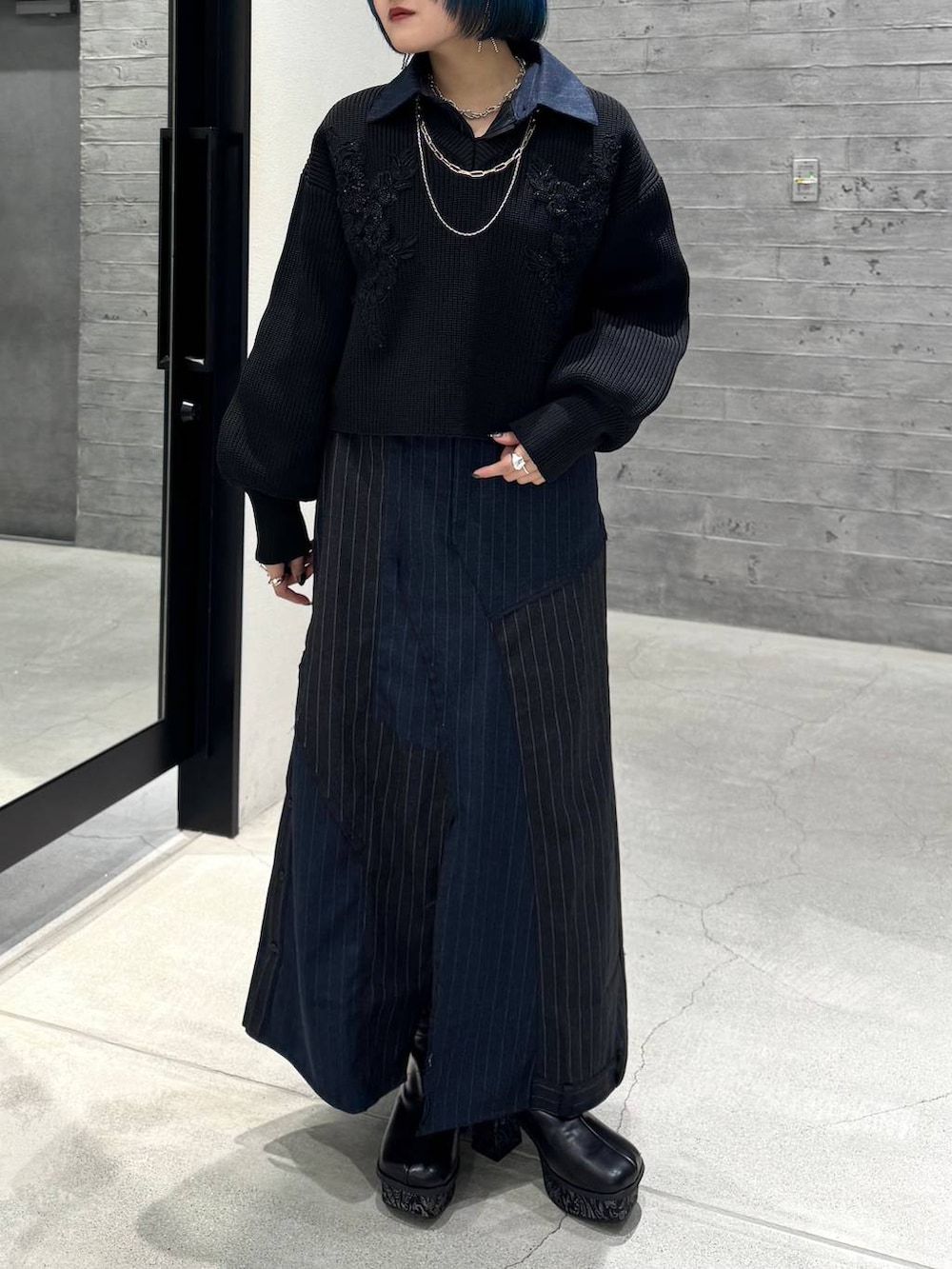 グレー系のブーツ、ブラック系のニット/セーター、ブルー系のスカートを着用したレディースの秋コーディネートの2枚目の写真