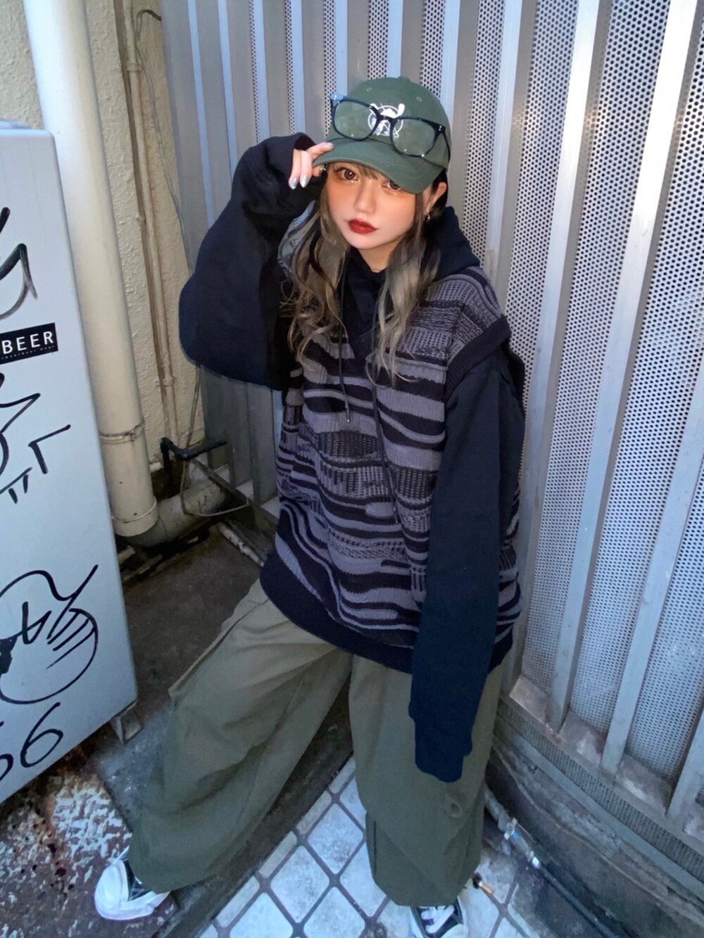 ブラック系のベスト、グリーン系のキャップ、ブラック系のメガネを着用したレディースの冬コーディネートの2枚目の写真