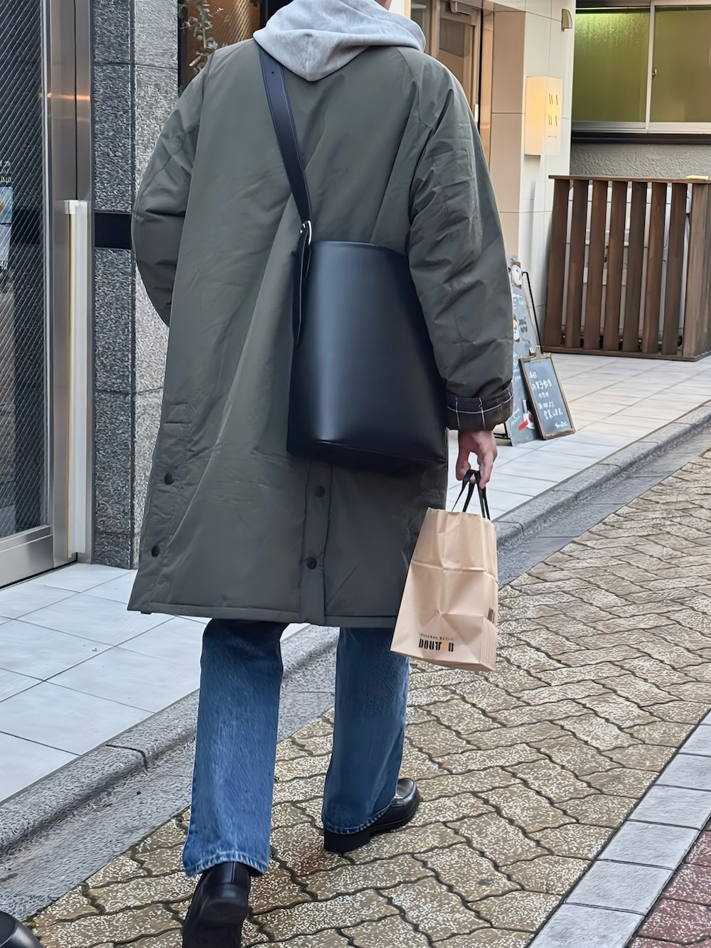 グリーン系のステンカラーコート、ブルー系のデニムパンツ、ブラック系のローファーを着用したメンズの春コーディネートの2枚目の写真