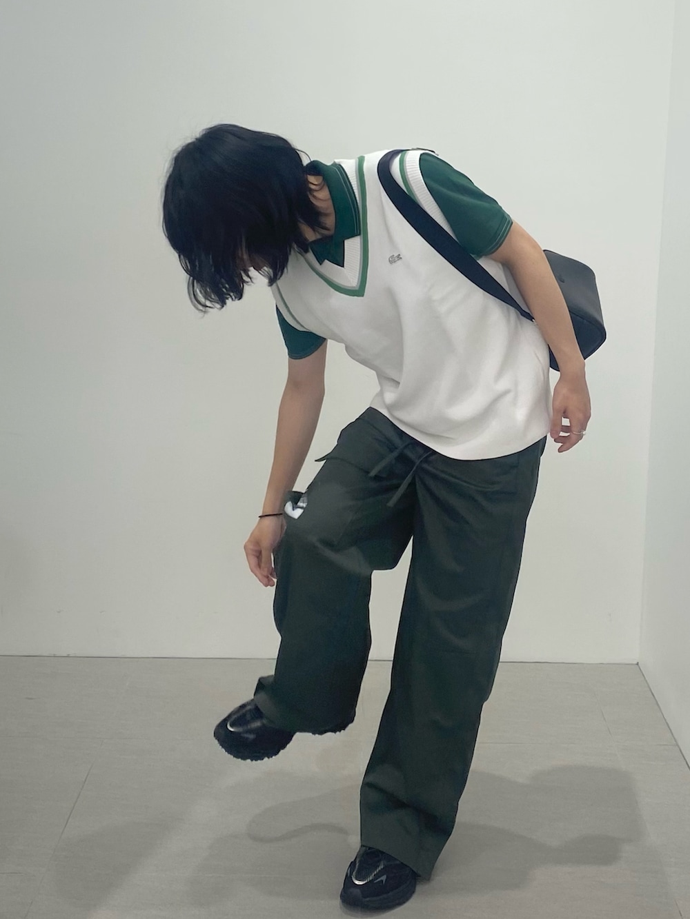 グリーン系のポロシャツ、ブラック系のショルダーバッグ、ホワイト系のベストを着用したメンズの春コーディネートの2枚目の写真