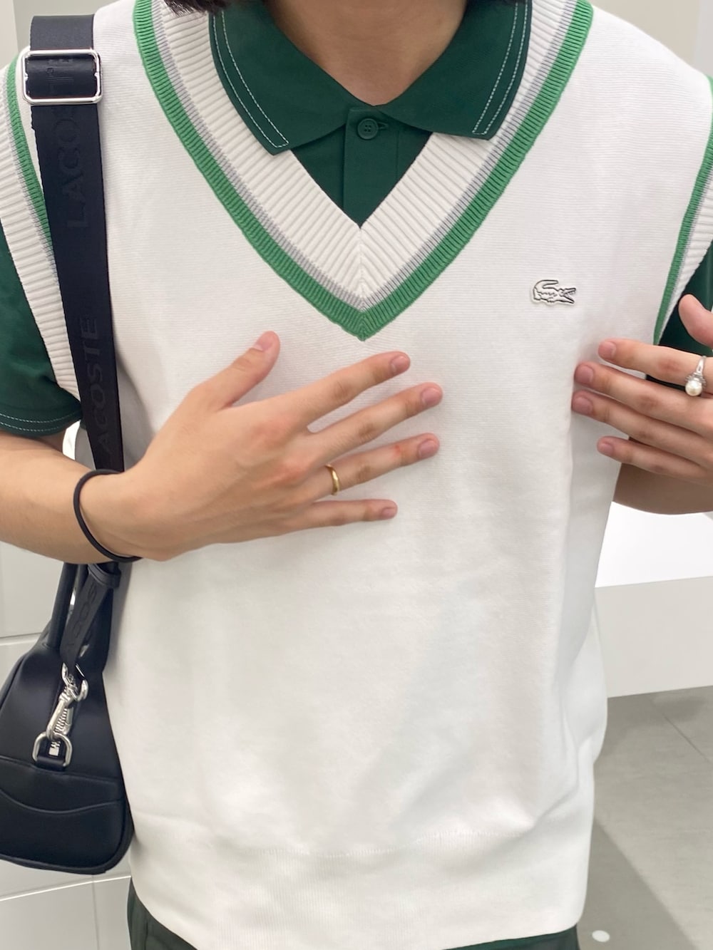 グリーン系のポロシャツ、ブラック系のショルダーバッグ、ホワイト系のベストを着用したメンズの春コーディネートの3枚目の写真