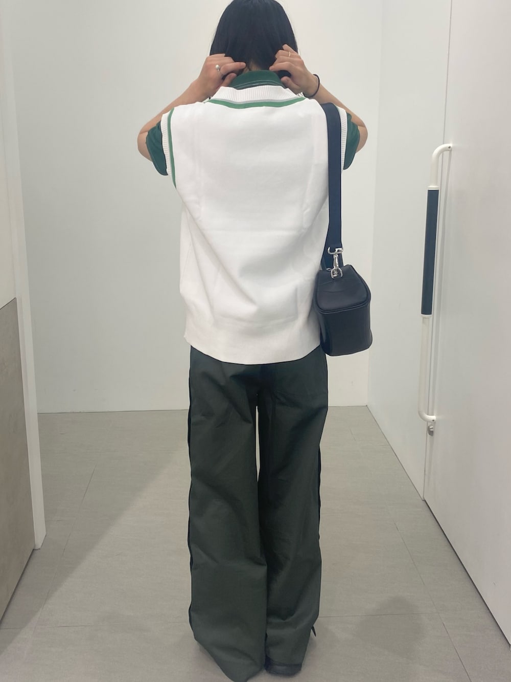 グリーン系のポロシャツ、ブラック系のショルダーバッグ、ホワイト系のベストを着用したメンズの春コーディネートの4枚目の写真