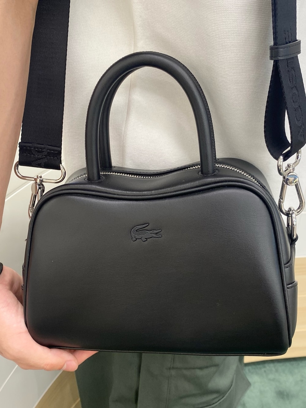 グリーン系のポロシャツ、ブラック系のショルダーバッグ、ホワイト系のベストを着用したメンズの春コーディネートの5枚目の写真