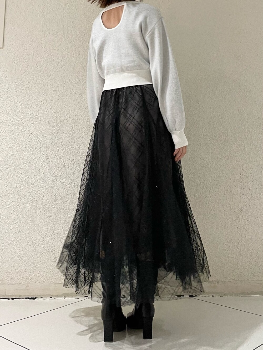 ブラック系のスカート、ホワイト系のニット/セーター、ブラック系のブーツを着用したレディースの冬コーディネートの3枚目の写真