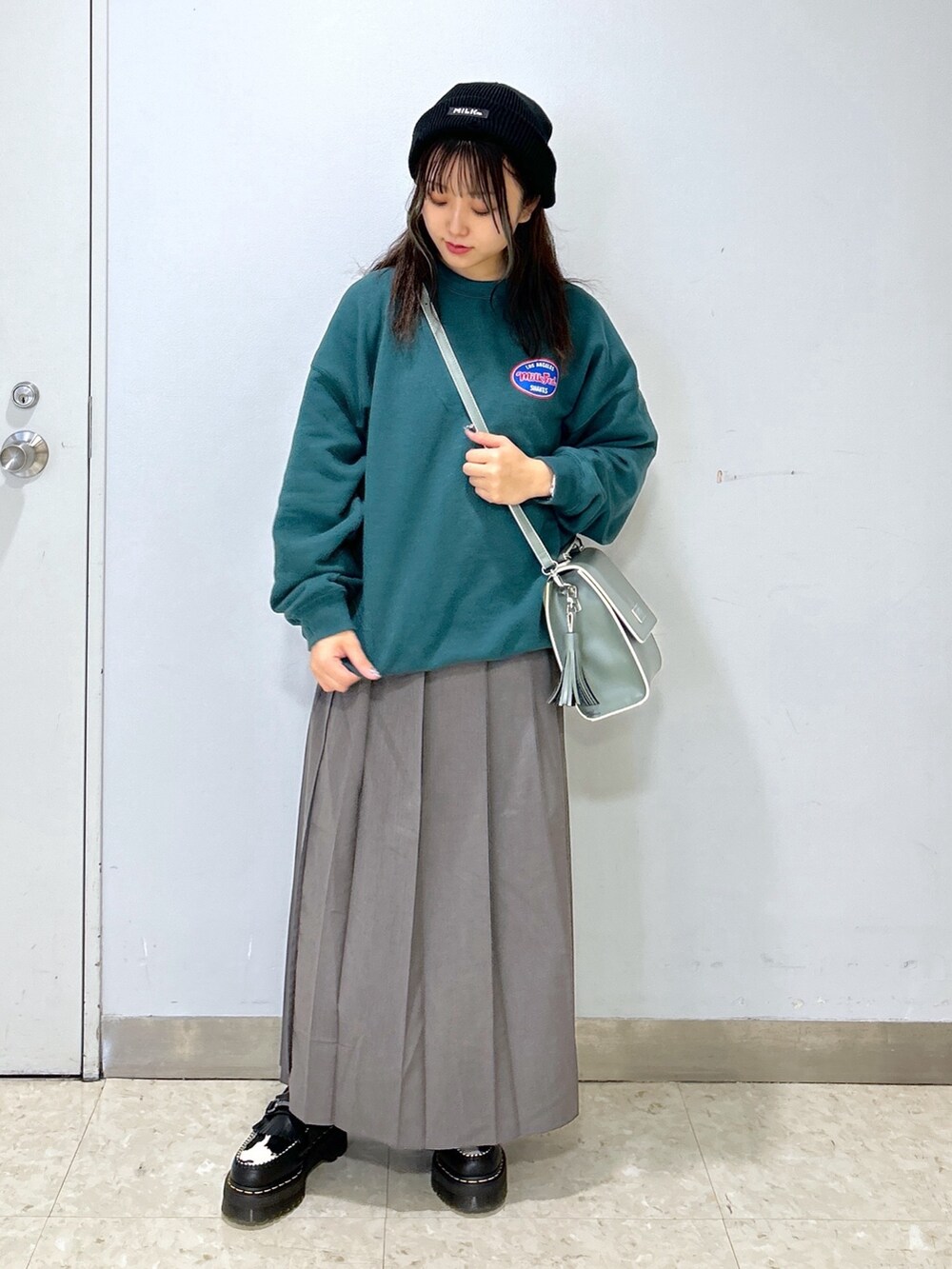グレー系のショルダーバッグ、グリーン系のスウェット、ブラック系のローファーを着用したレディースの冬コーディネートの2枚目の写真