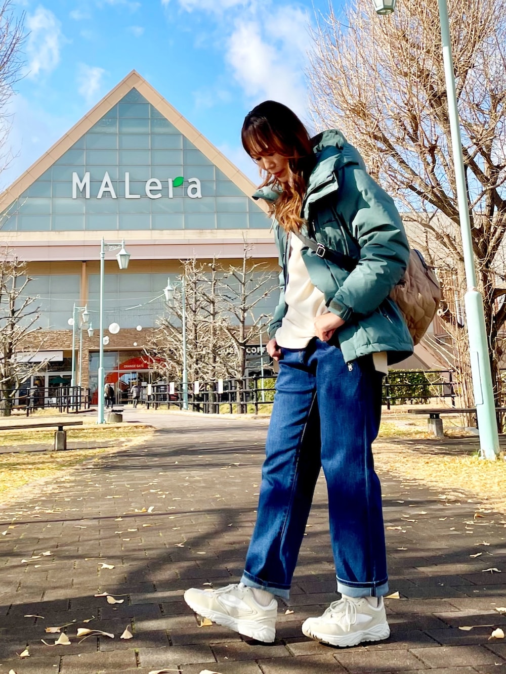 グリーン系のダウンジャケット/コート、ホワイト系のチュニック、ブルー系のデニムパンツを着用したレディースの冬コーディネートの2枚目の写真