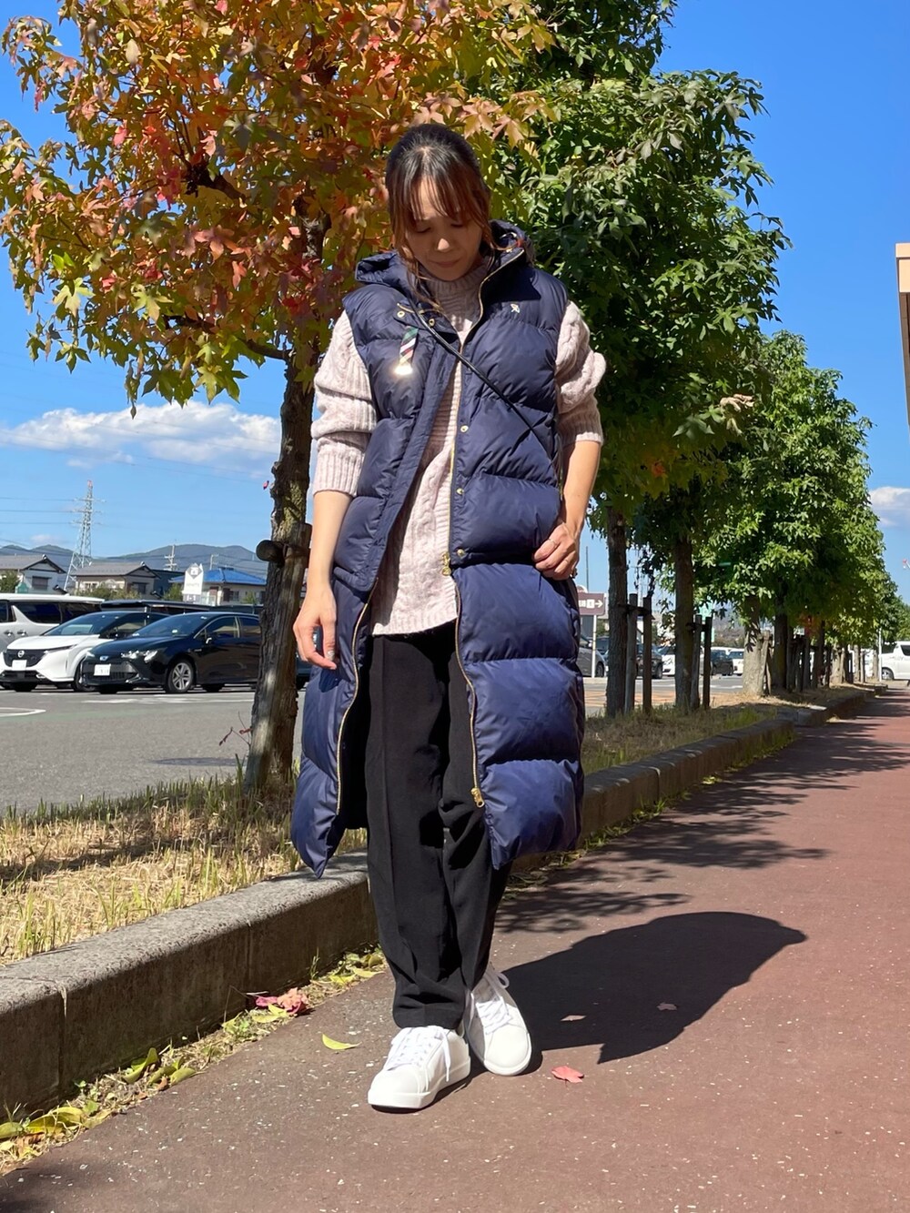 ピンク系のニット/セーター、ブルー系のダウンベスト、ブラック系のショルダーバッグを着用したレディースの秋コーディネートの2枚目の写真