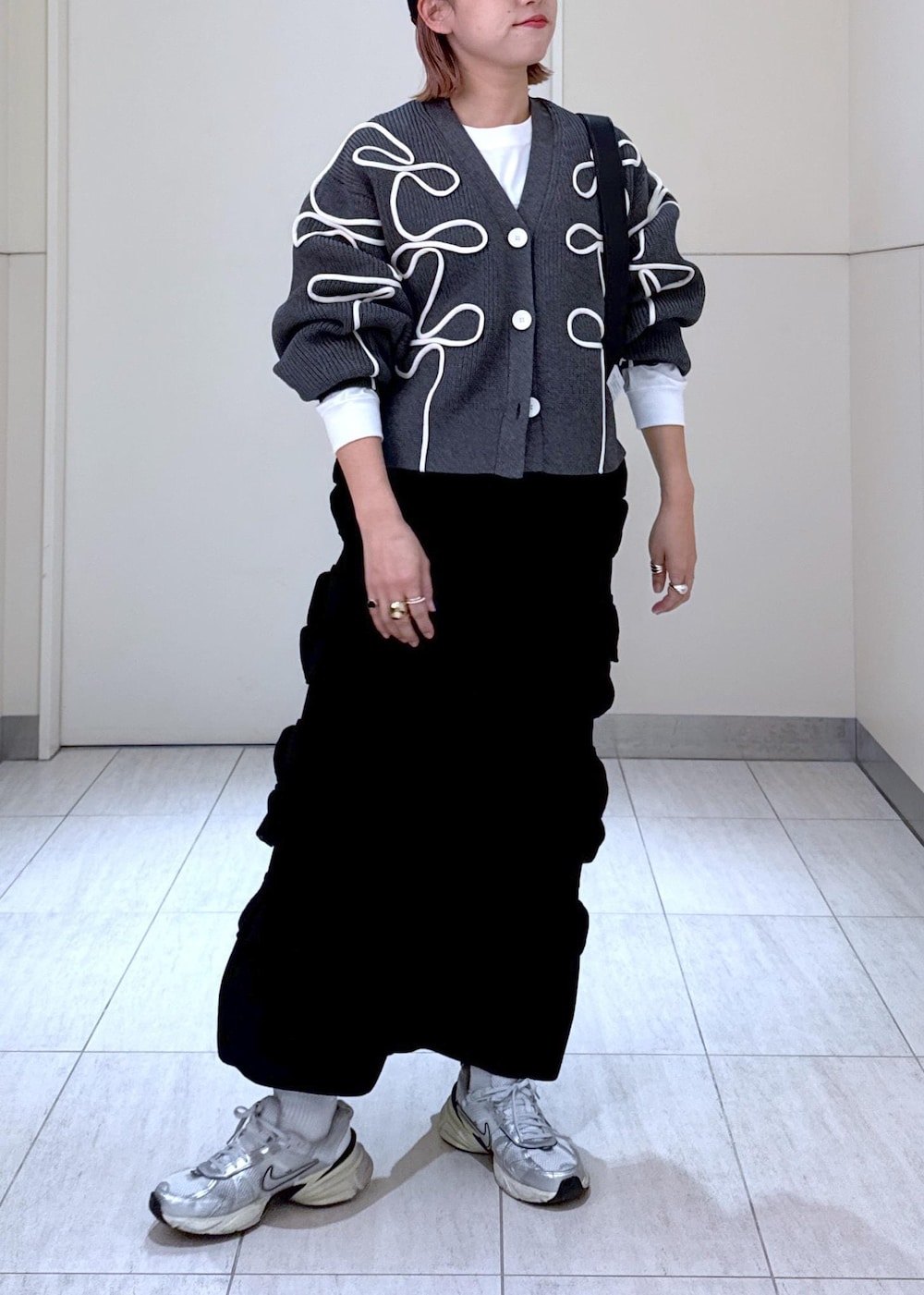 ホワイト系のTシャツ/カットソー、ブラック系のスカート、グレー系のカーディガン/ボレロを着用したレディースの秋コーディネートの2枚目の写真