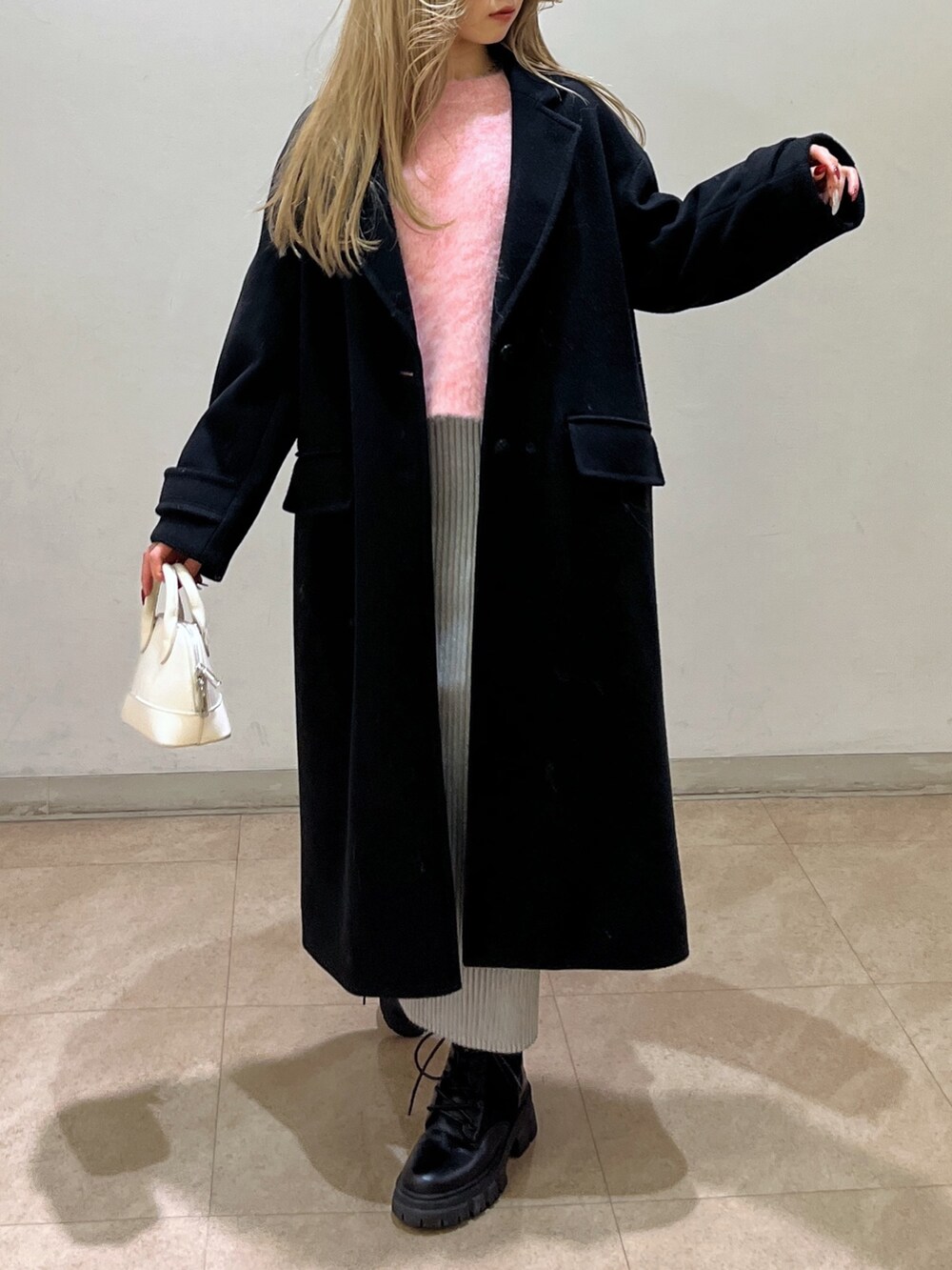 ピンク系のニット/セーター、ブラック系のチェスターコート、ブラック系のブーツを着用したレディースの冬コーディネートの7枚目の写真