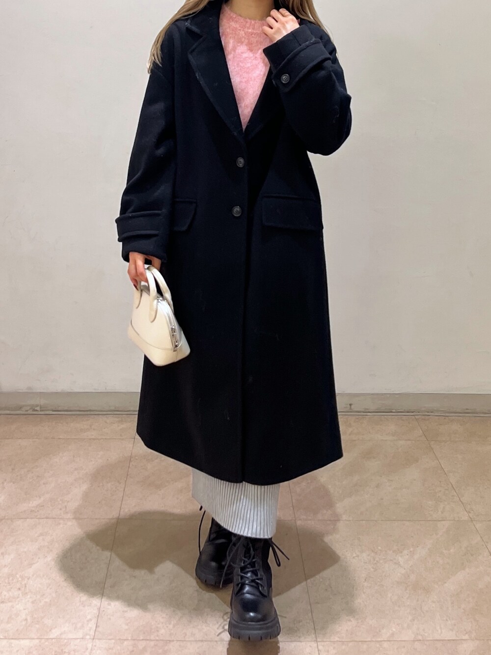 ピンク系のニット/セーター、ブラック系のチェスターコート、ブラック系のブーツを着用したレディースの冬コーディネートの4枚目の写真