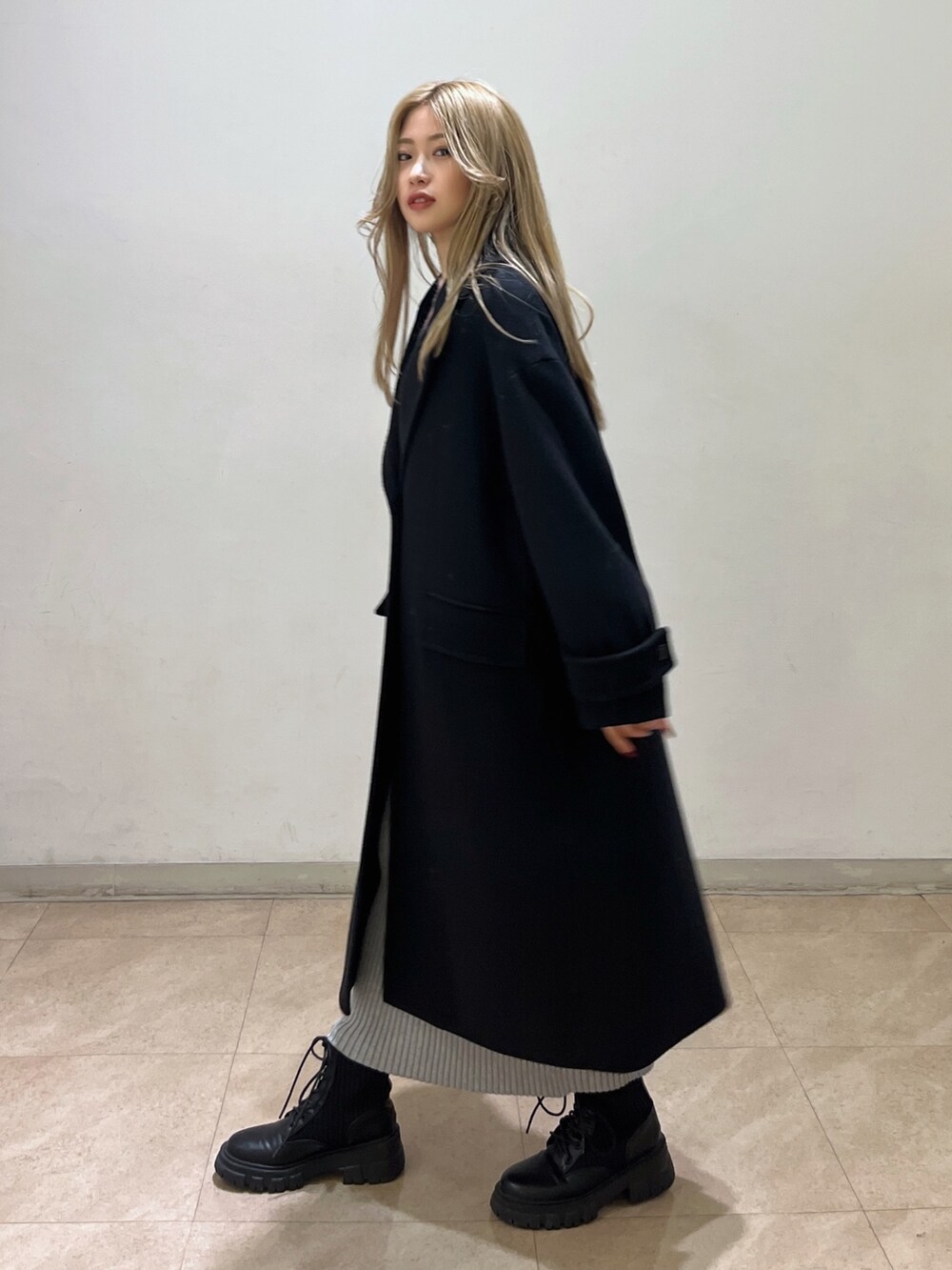 ピンク系のニット/セーター、ブラック系のチェスターコート、ブラック系のブーツを着用したレディースの冬コーディネートの2枚目の写真