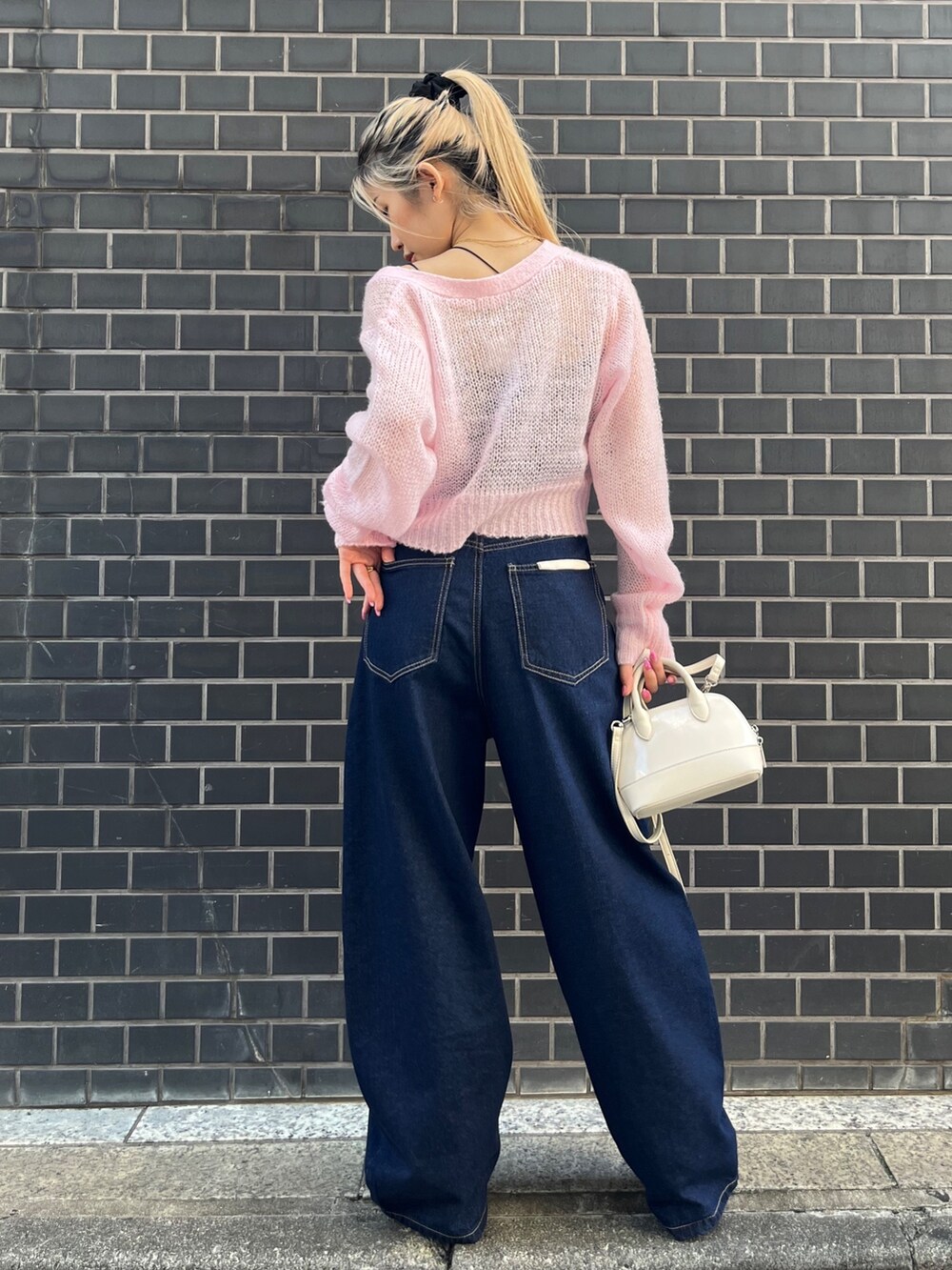 ブルー系のデニムパンツ、ホワイト系のショルダーバッグ、ピンク系のカーディガン/ボレロを着用したレディースの秋コーディネートの4枚目の写真