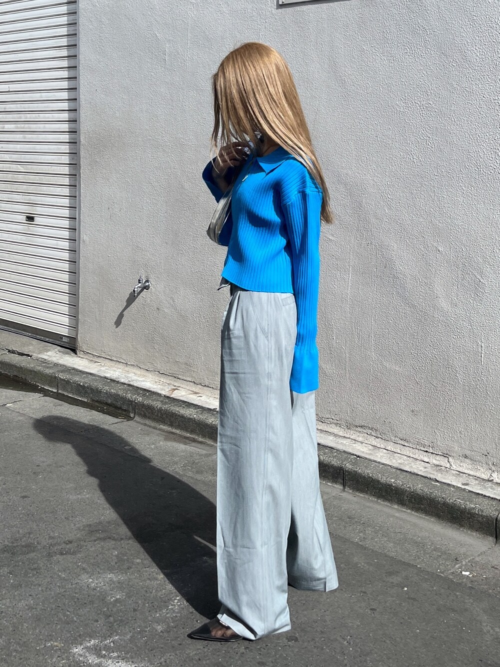 ブルー系のニット/セーター、シルバー系のショルダーバッグ、グレー系のスラックスを着用したレディースの春コーディネートの2枚目の写真