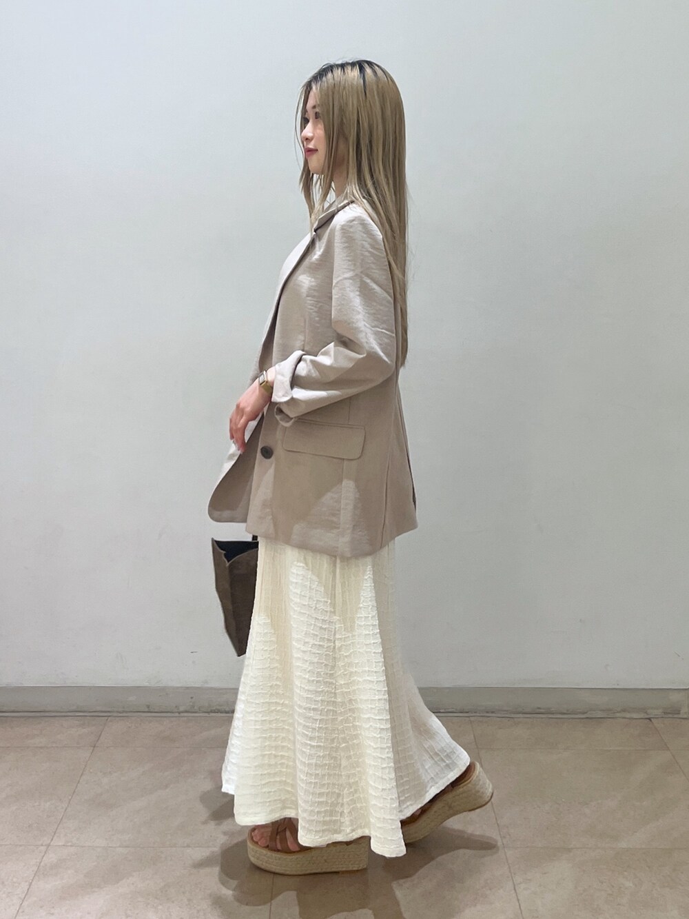 ベージュ系のテーラードジャケット、ブラウン系のショルダーバッグ、ホワイト系のワンピースを着用したレディースの春コーディネートの2枚目の写真