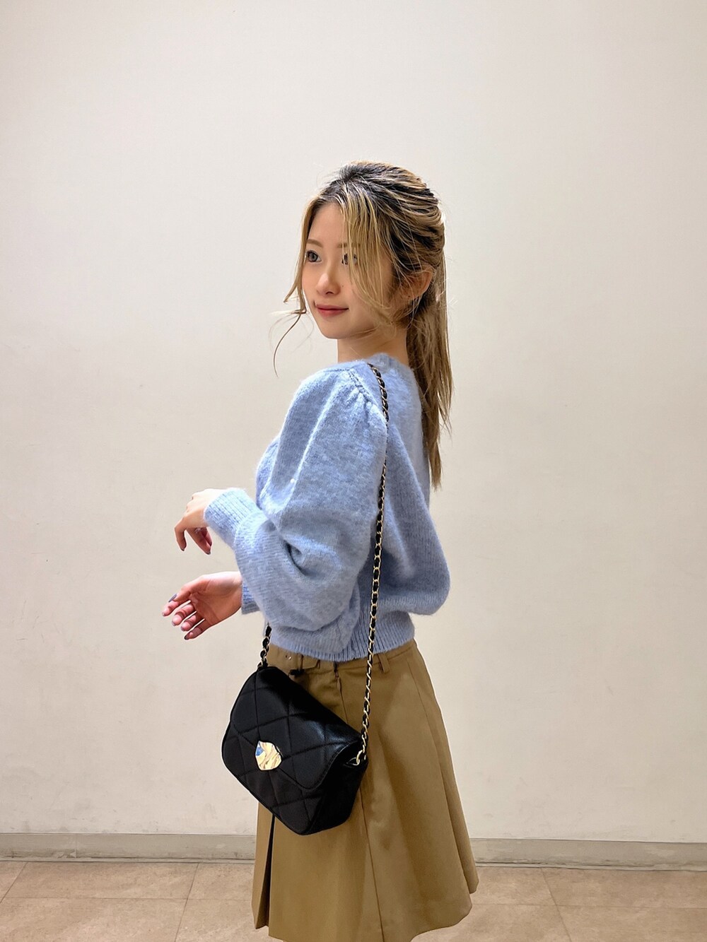 ブルー系のニット/セーター、ブラック系のショルダーバッグ、ベージュ系のスカートを着用したレディースの冬コーディネートの8枚目の写真