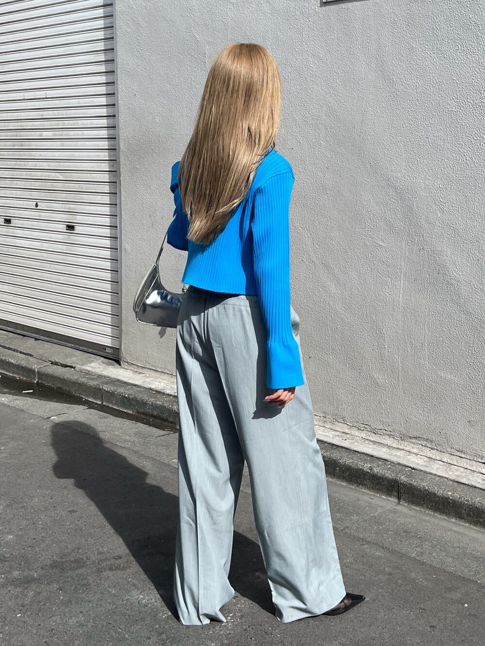 ブルー系のニット/セーター、シルバー系のショルダーバッグ、グレー系のスラックスを着用したレディースの春コーディネートの3枚目の写真