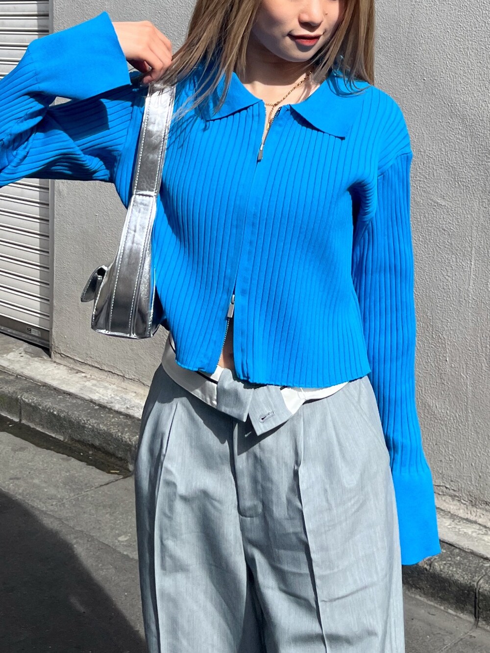 ブルー系のニット/セーター、シルバー系のショルダーバッグ、グレー系のスラックスを着用したレディースの春コーディネートの5枚目の写真