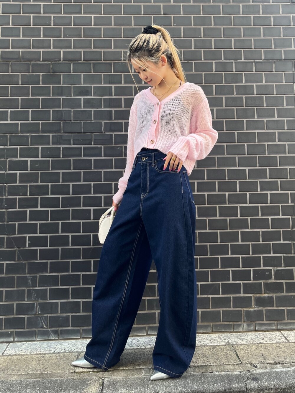 ブルー系のデニムパンツ、ホワイト系のショルダーバッグ、ピンク系のカーディガン/ボレロを着用したレディースの秋コーディネートの2枚目の写真