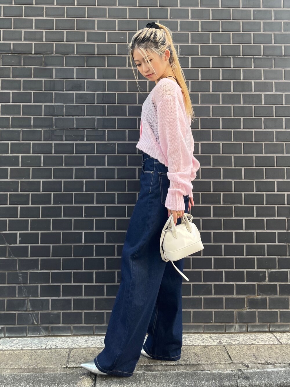 ブルー系のデニムパンツ、ホワイト系のショルダーバッグ、ピンク系のカーディガン/ボレロを着用したレディースの秋コーディネートの3枚目の写真