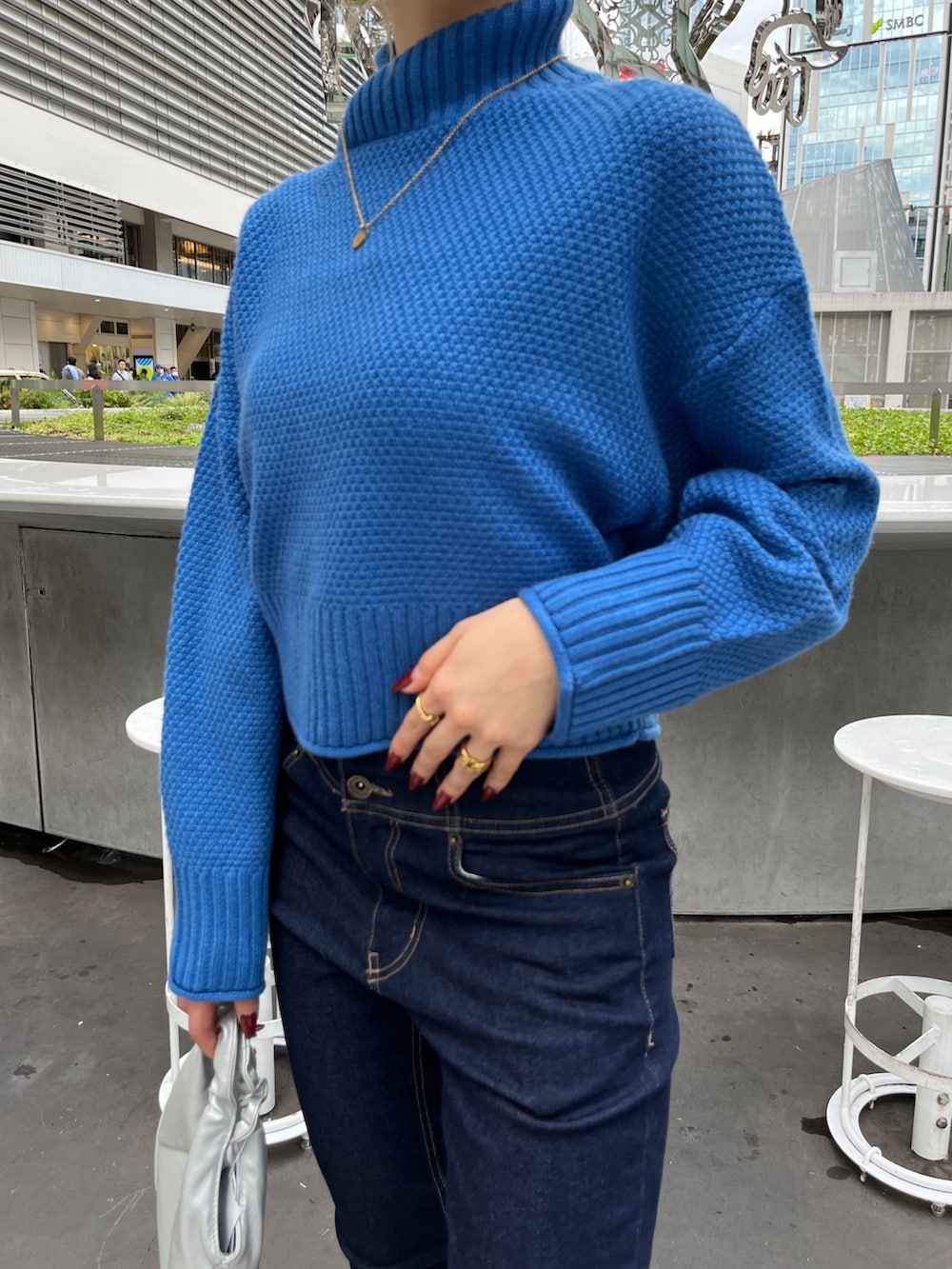 ブルー系のニット/セーター、ブルー系のデニムパンツ、シルバー系のショルダーバッグを着用したレディースの秋コーディネートの5枚目の写真