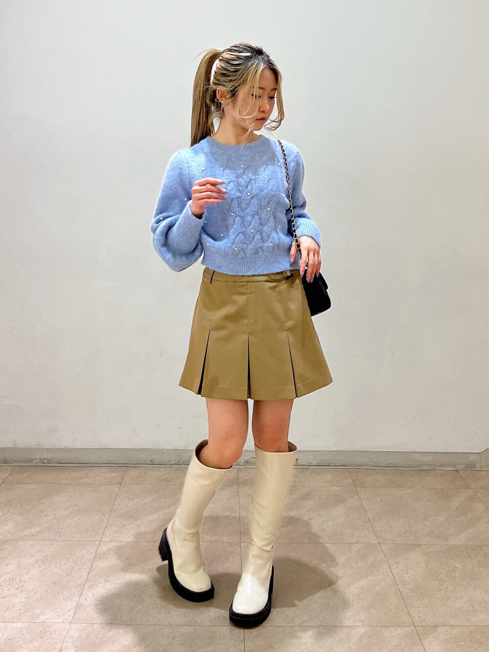 ブルー系のニット/セーター、ブラック系のショルダーバッグ、ベージュ系のスカートを着用したレディースの冬コーディネートの2枚目の写真