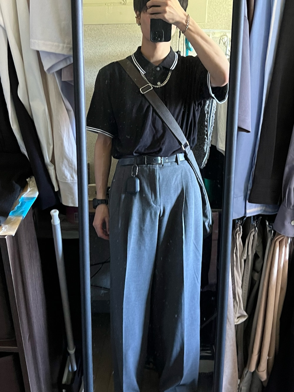 ブラック系のポロシャツ、グレー系のショルダーバッグ、グレー系のスラックスを着用したメンズの夏コーディネートの2枚目の写真
