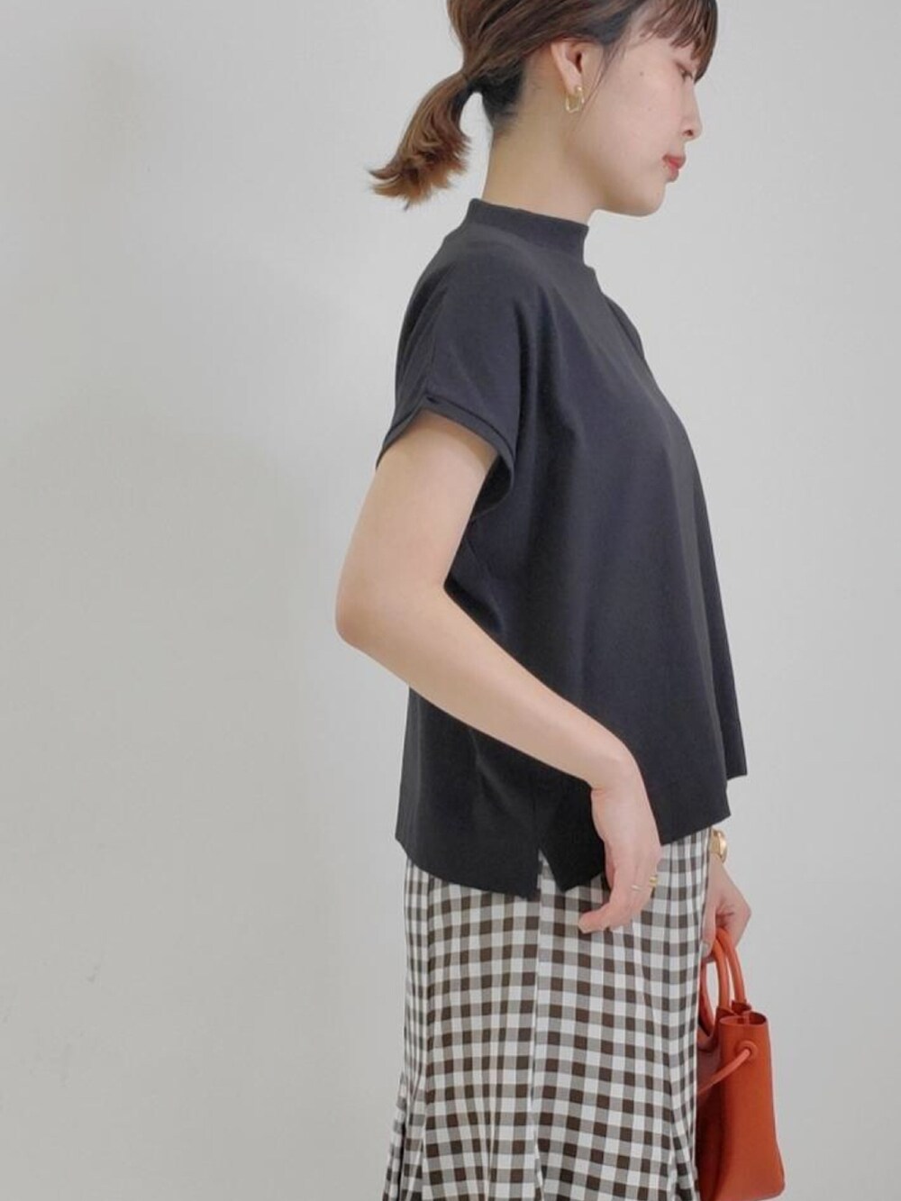 オレンジ系のショルダーバッグ、ブラウン系のスカート、ブラック系のTシャツ/カットソーを着用したレディースの夏コーディネートの2枚目の写真