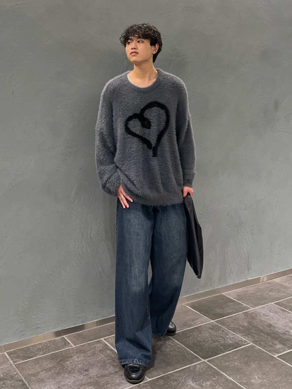グレー系のニット/セーター、ブラック系のトートバッグ、ブルー系のデニムパンツを着用したメンズの秋コーディネートの3枚目の写真