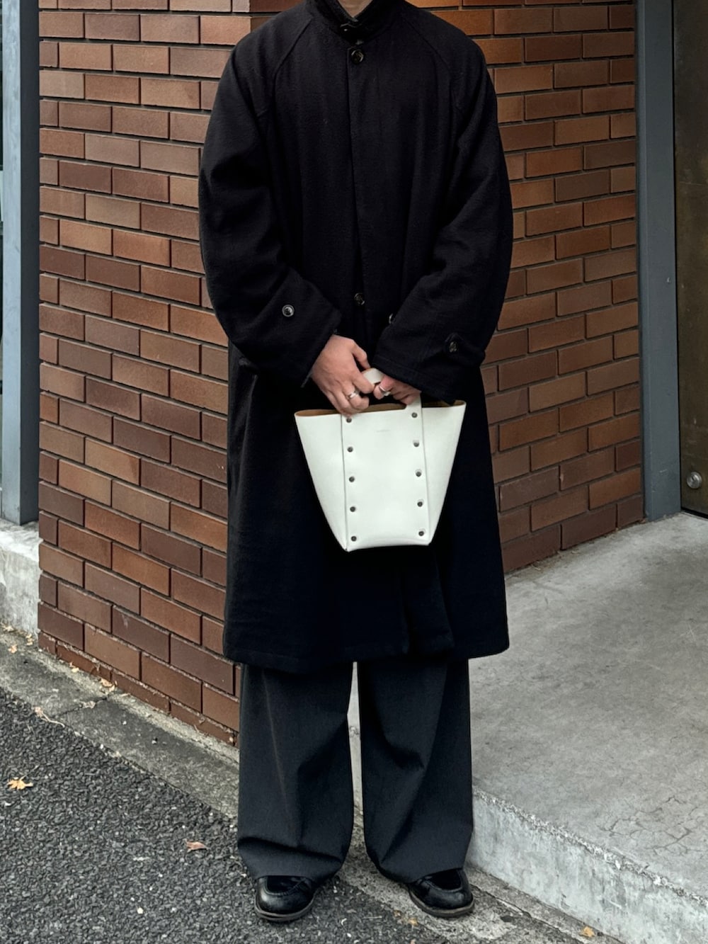 ブラック系のステンカラーコート、ホワイト系のハンドバッグ、グレー系のスラックスを着用したメンズの冬コーディネートの3枚目の写真
