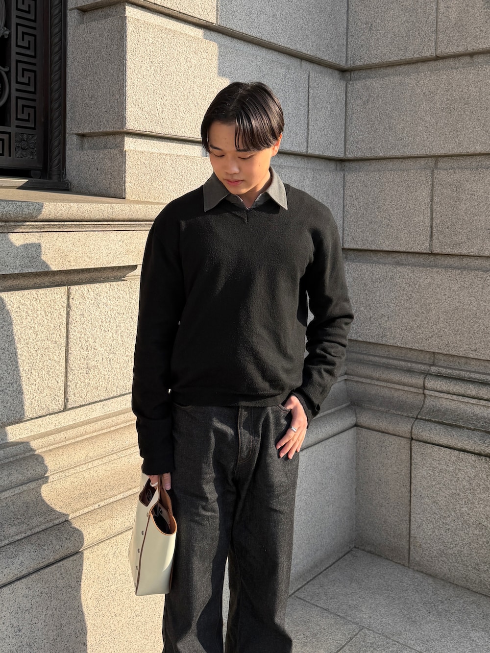 ブラック系のデニムパンツ、ホワイト系のハンドバッグ、ブラック系のニット/セーターを着用したメンズの春コーディネートの3枚目の写真