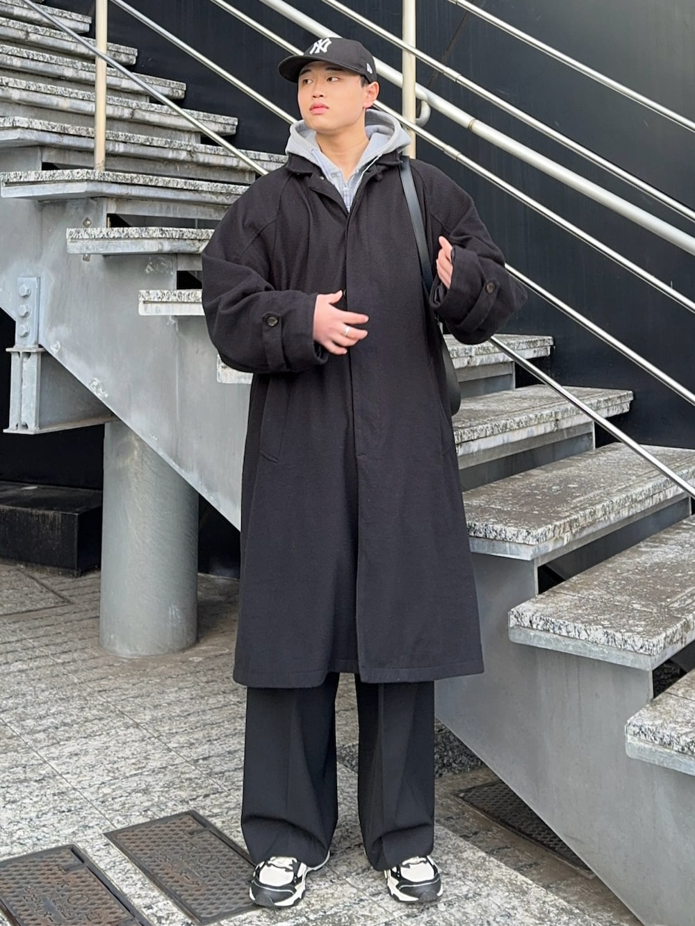 ブラック系のステンカラーコート、ブラック系のショルダーバッグ、グレー系のパーカーを着用したメンズの冬コーディネートの2枚目の写真