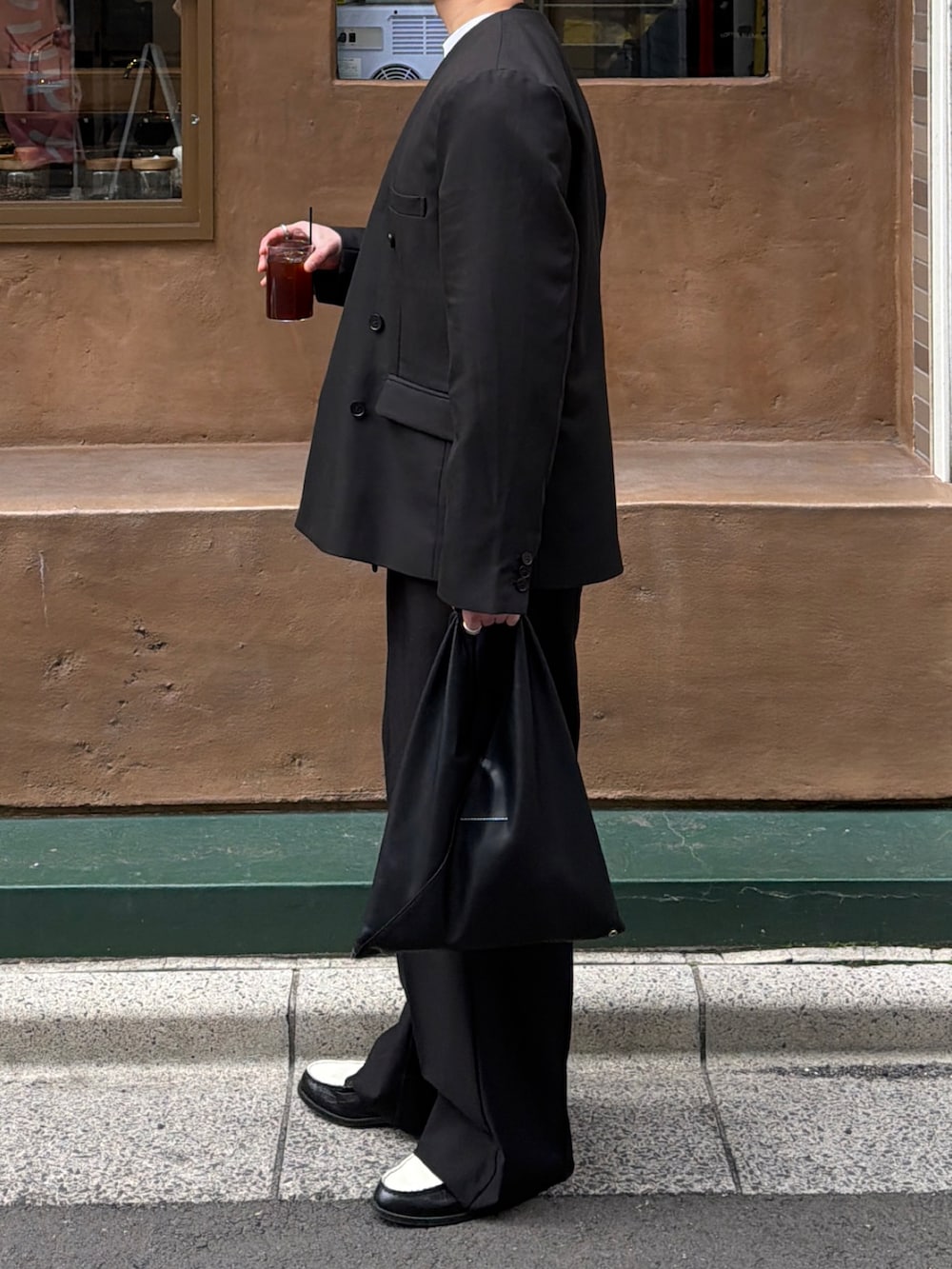 ブラック系のテーラードジャケット、ブルー系のニット/セーター、ブラック系のトートバッグを着用したメンズの春コーディネートの3枚目の写真